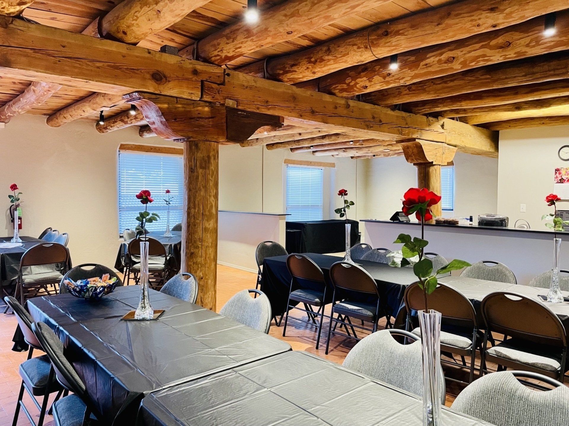 Large room with exposed wooden beams, tables set with roses, and chairs; neutral setting.