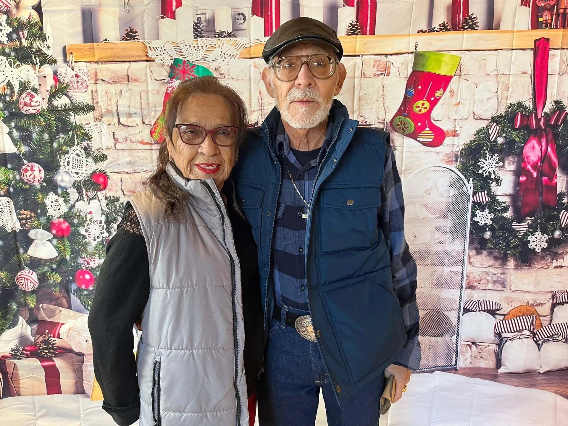 Couple posing in front of a Christmas backdrop with a tree, gifts, and fireplace.