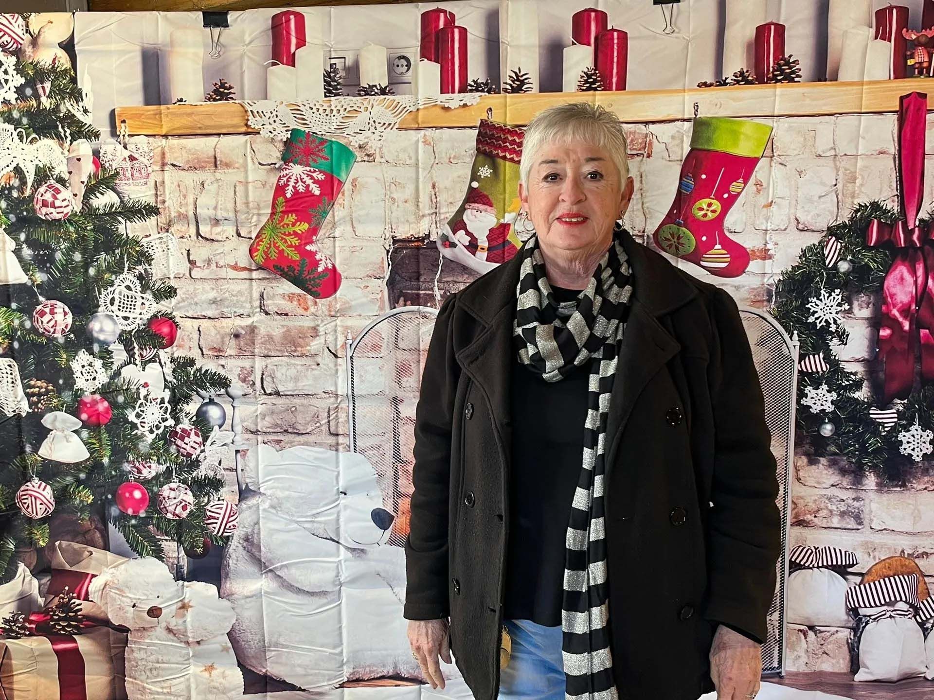 Woman in a dark coat and scarf posing in front of a Christmas backdrop.