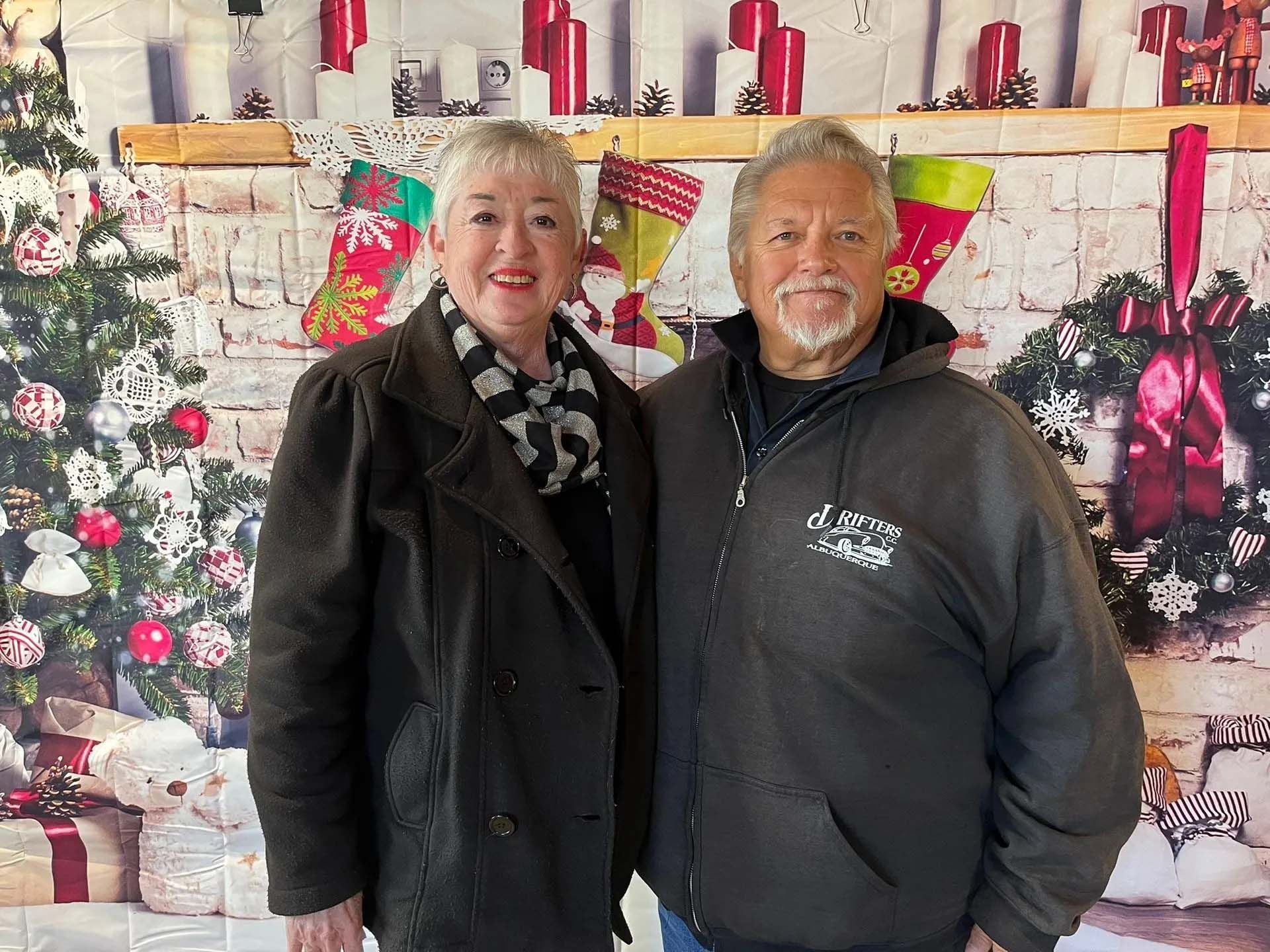 Couple posing in front of a Christmas backdrop with a tree, stockings, and wreath.