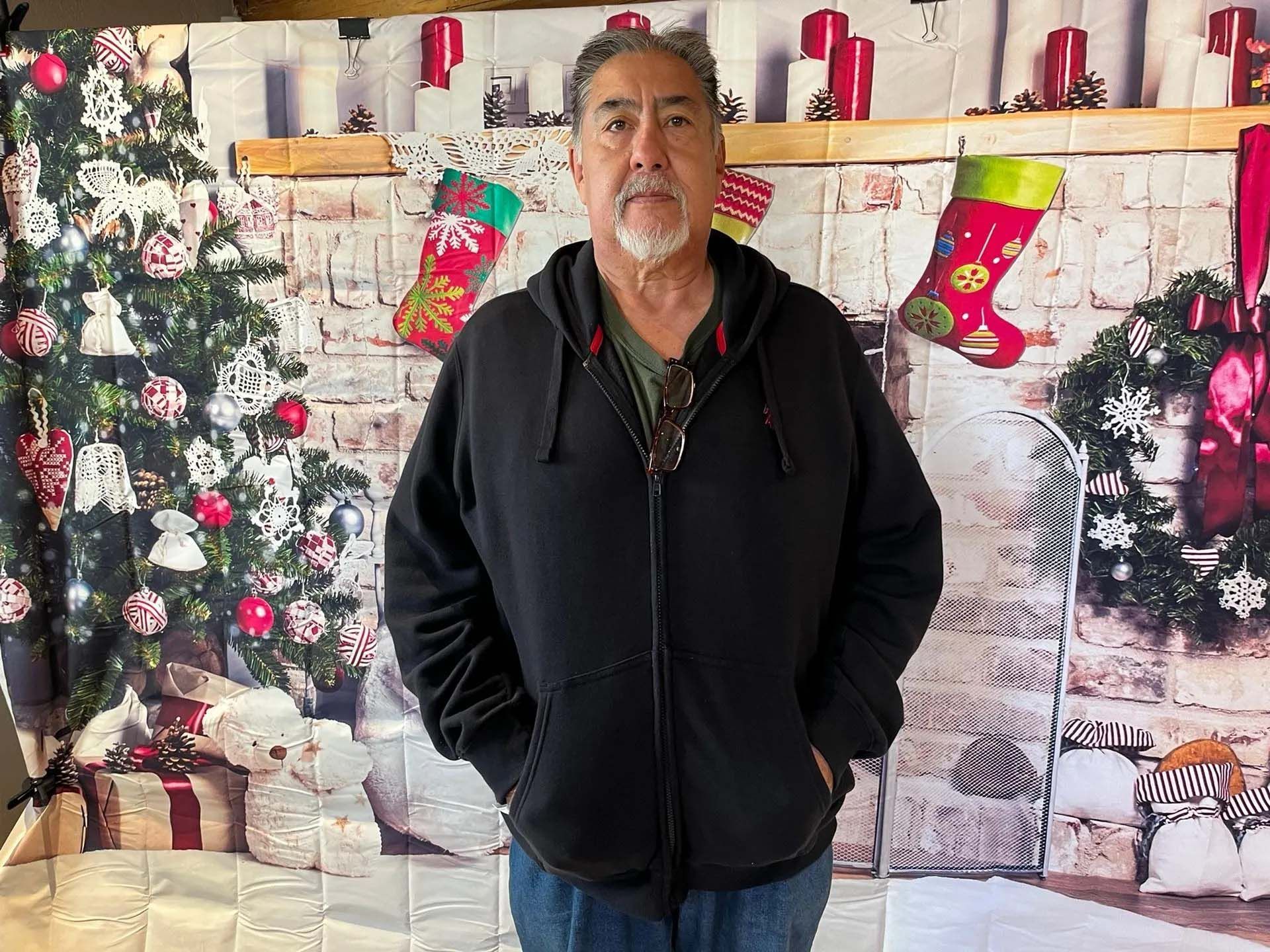 Man in black hoodie and jeans posing in front of a Christmas backdrop.