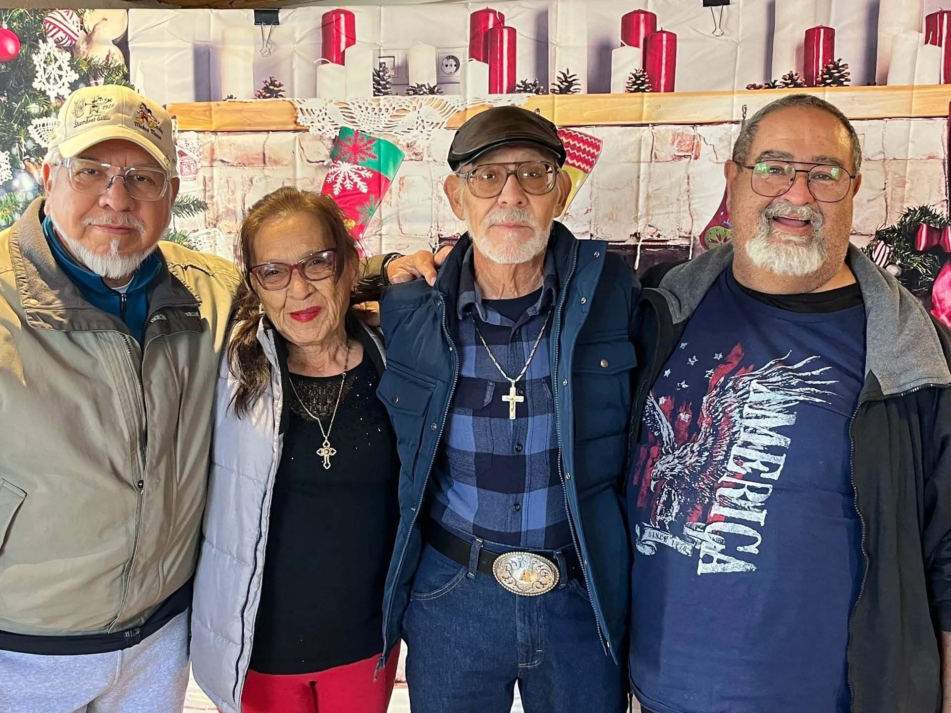 Four people stand together; Christmas decorations in background. Two men wear hats, all smiling.