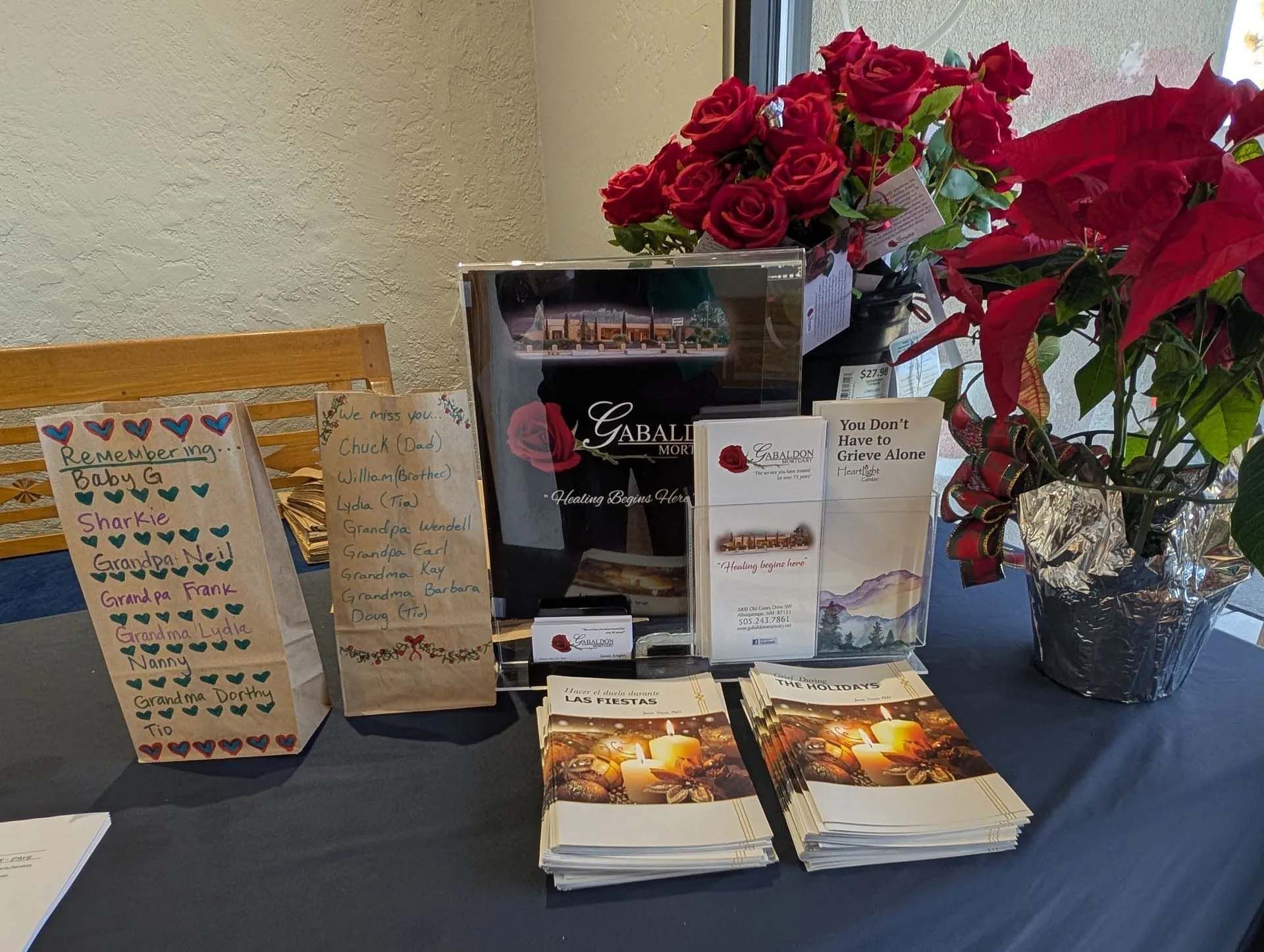 Display table with promotional materials, flowers, and two paper bags with writing on them.