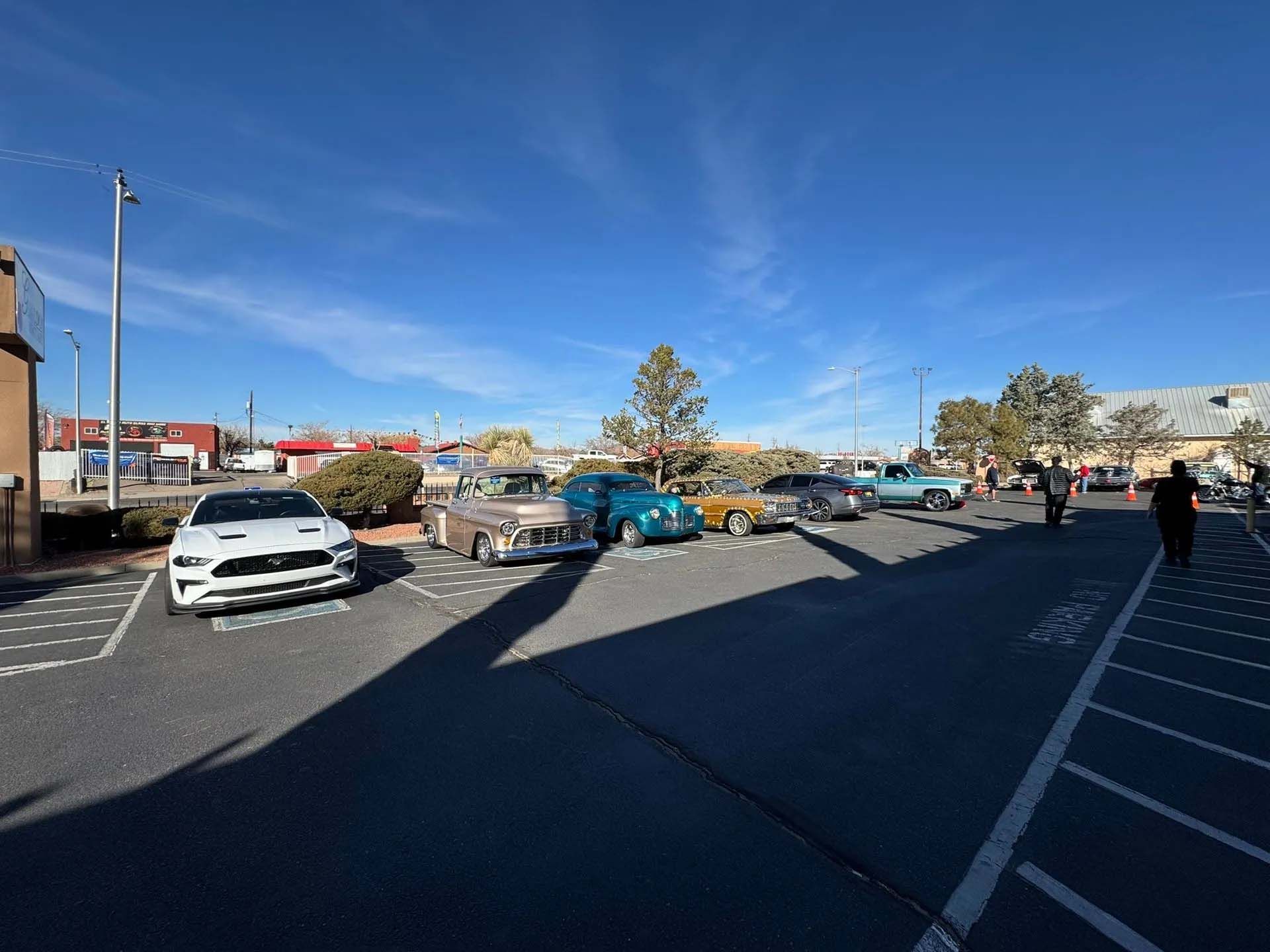 Classic cars parked outdoors under a blue sky, some people visible nearby.