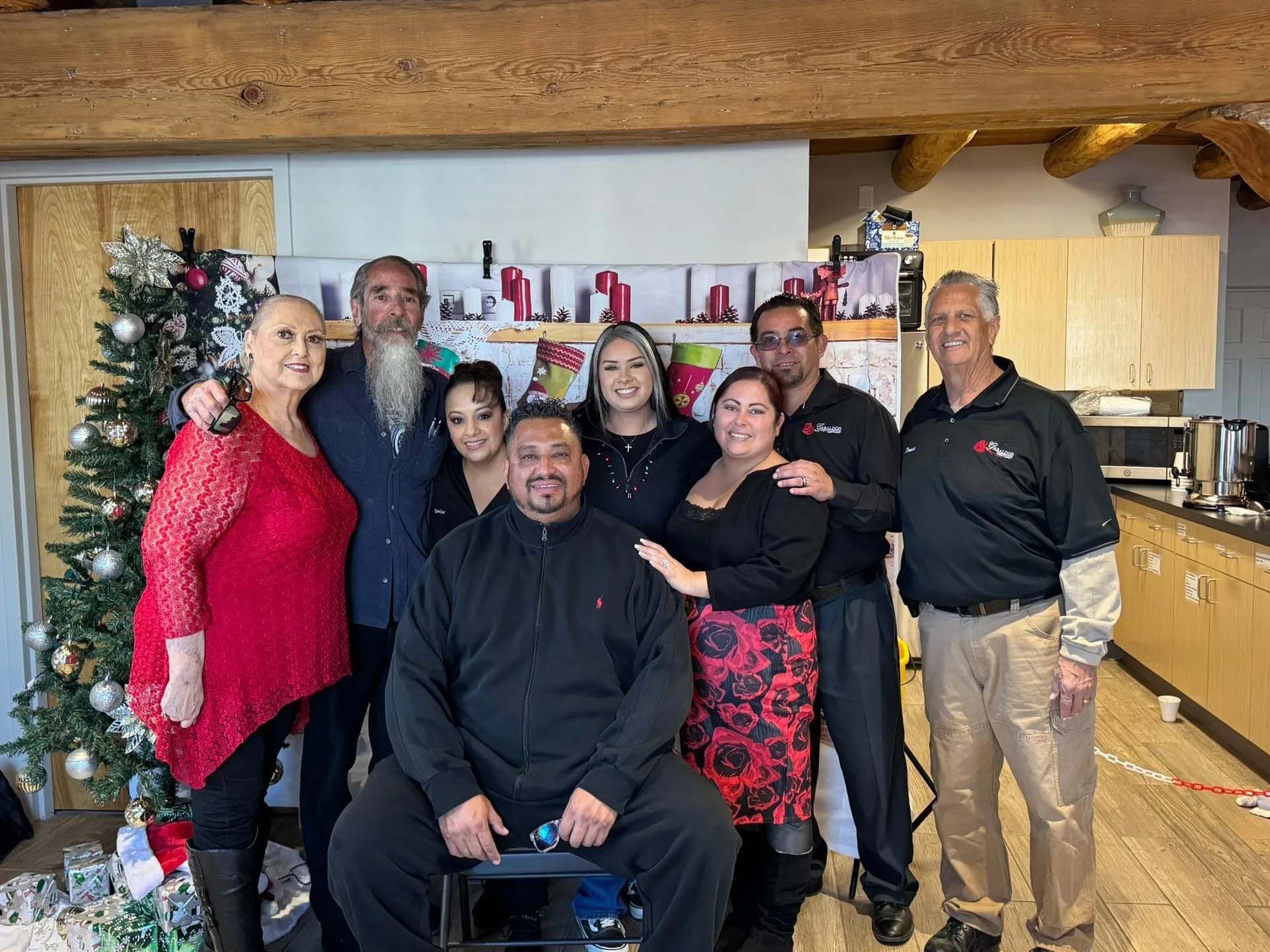 Group of people posing near Christmas tree and kitchen, smiling.