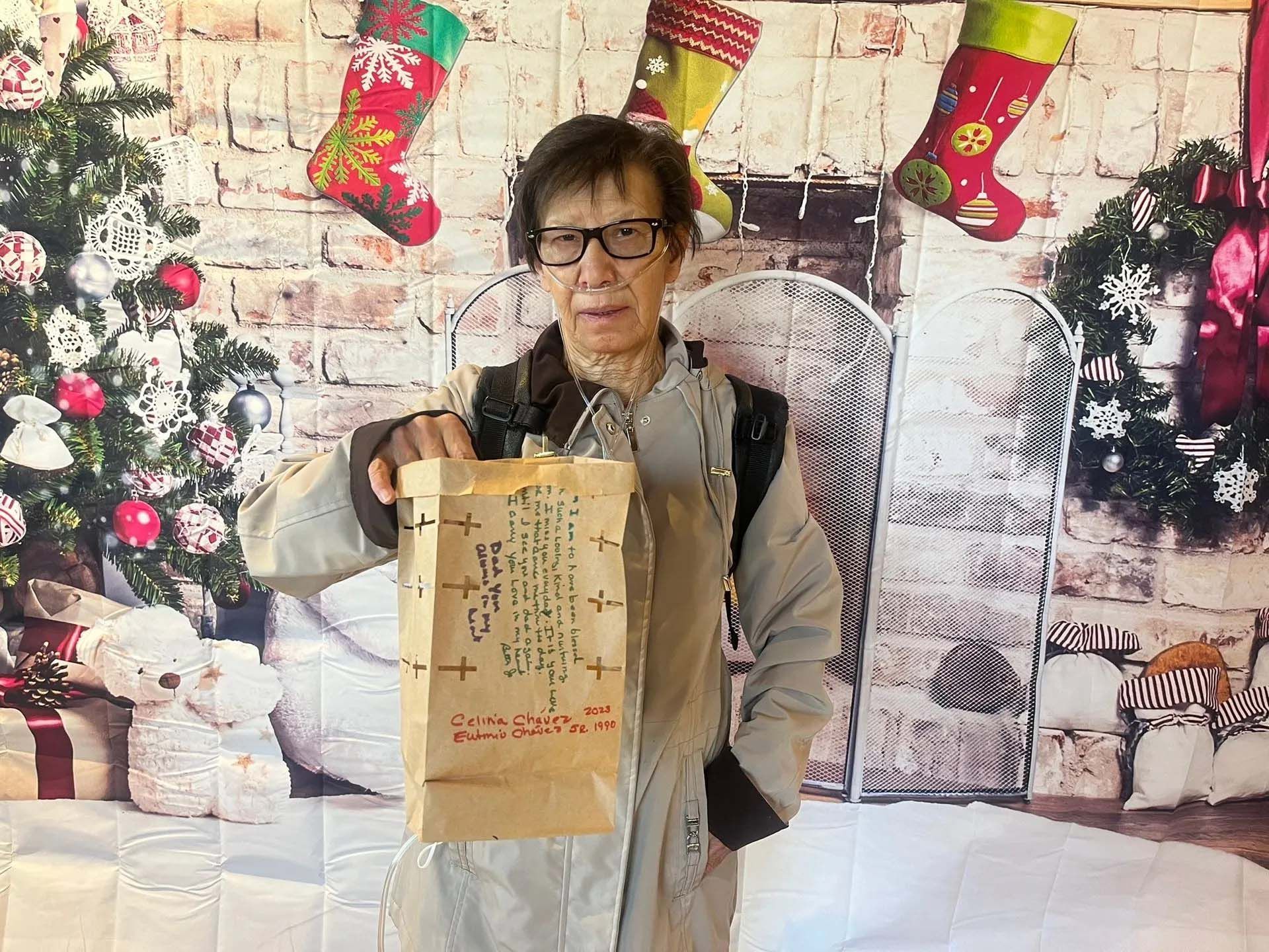 Person holding a brown paper bag in front of a Christmas backdrop.