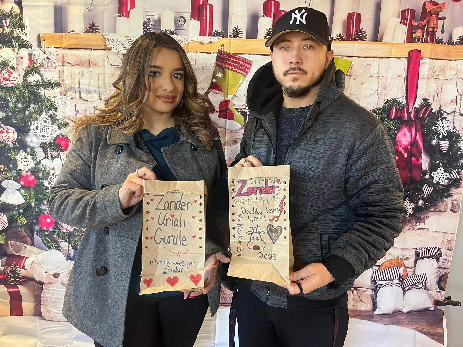 Couple holding decorated paper bags in front of Christmas backdrop.