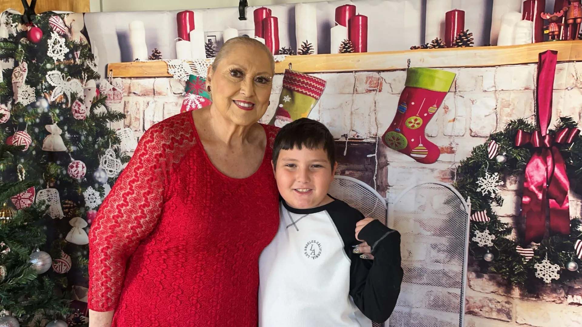 Woman in red dress and boy in baseball shirt pose in front of a Christmas backdrop.