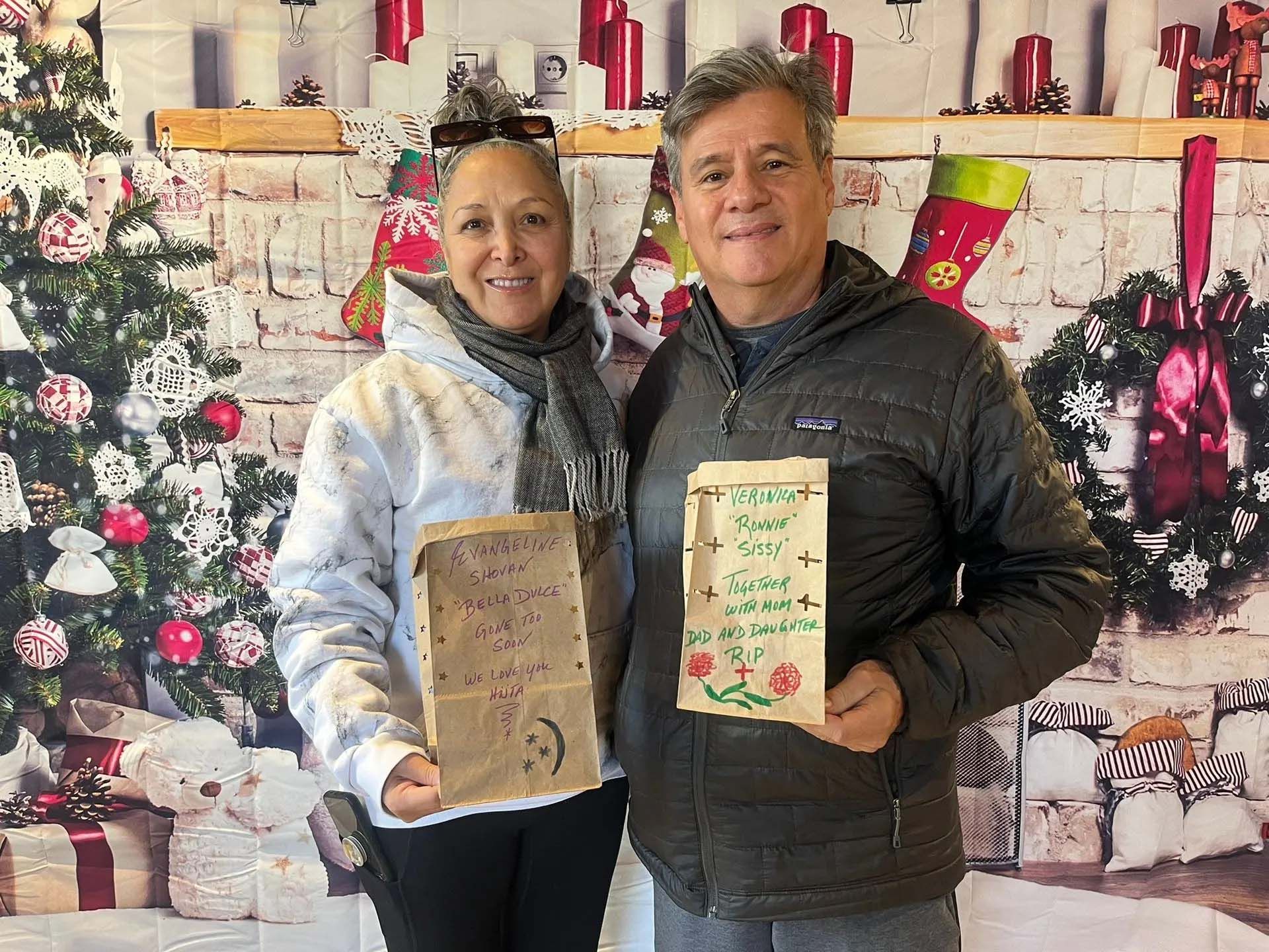 Two people holding decorated paper bags, smiling, in front of Christmas decorations.