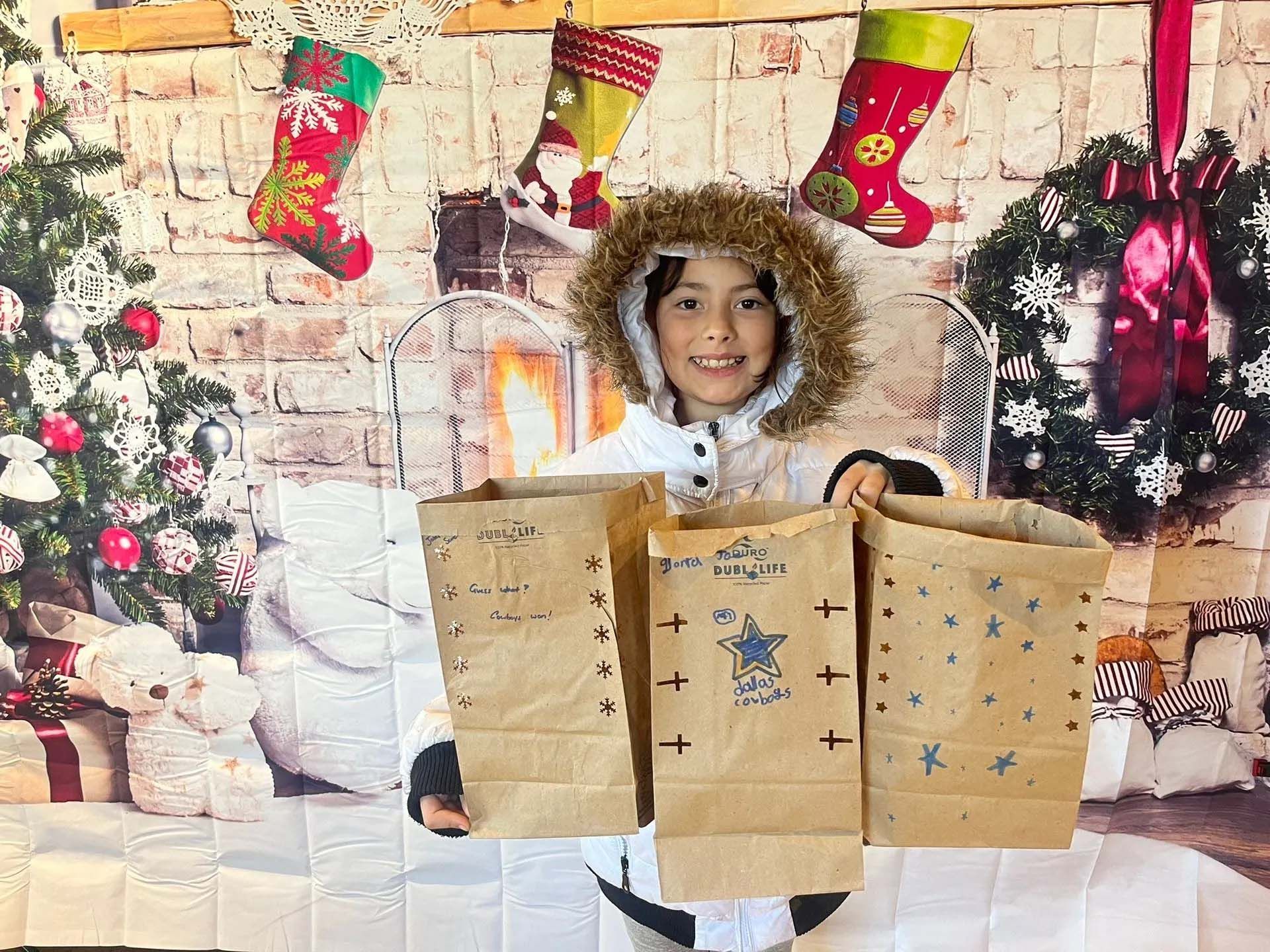Person holding three decorated paper bags in front of a Christmas backdrop.