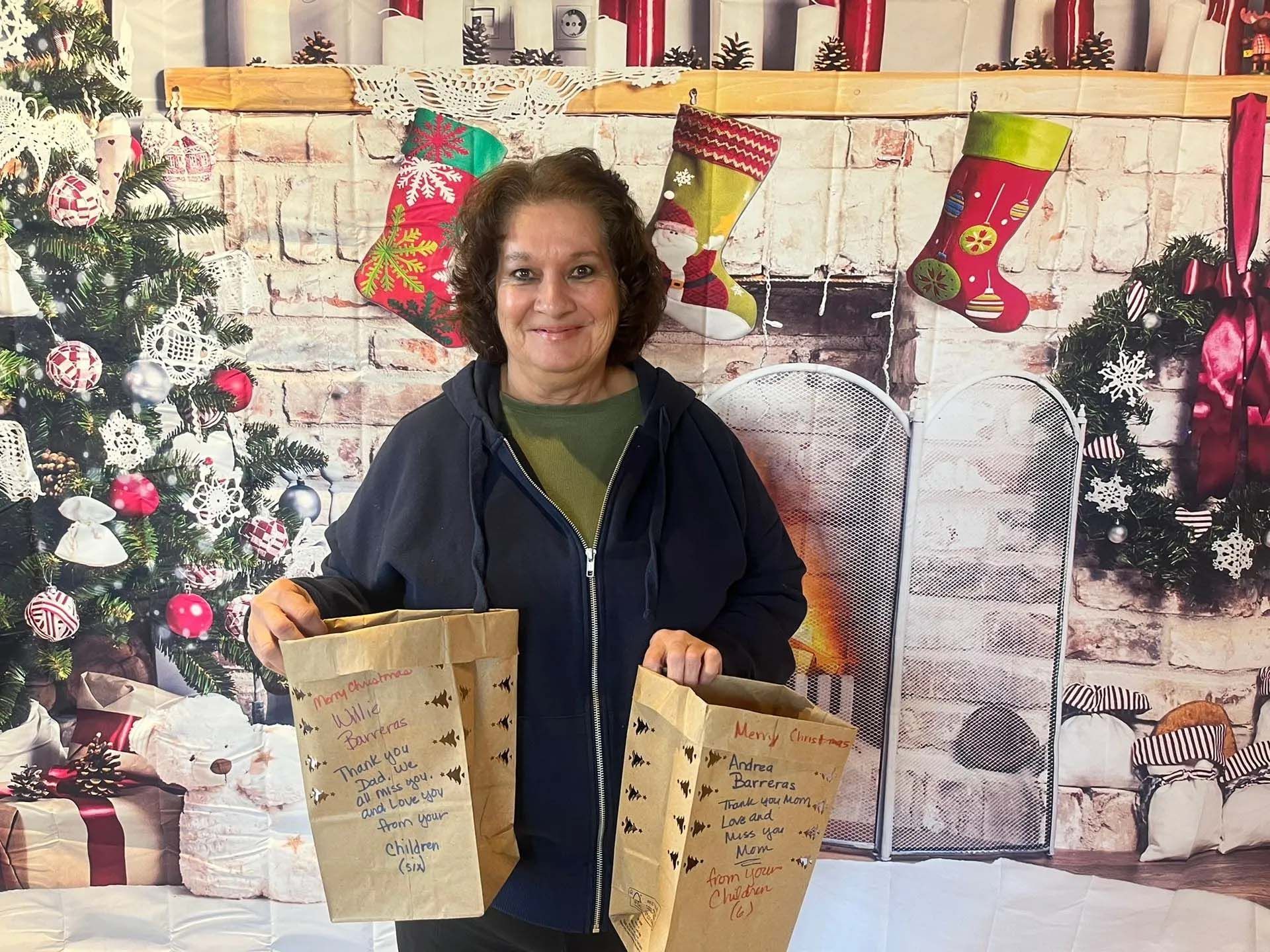 Woman holds two brown paper bags with writing, in front of a Christmas backdrop.