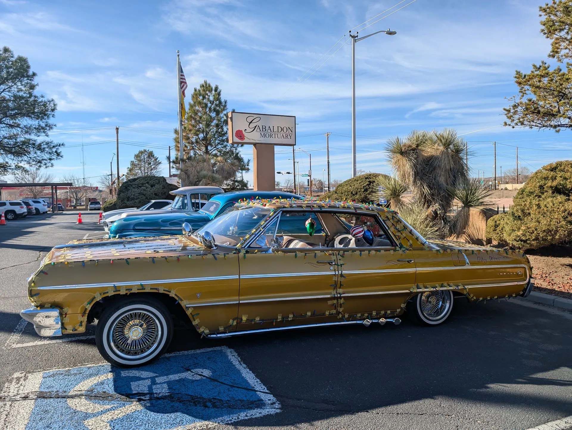 Gold lowrider car with custom details parked outside a restaurant on a sunny day.