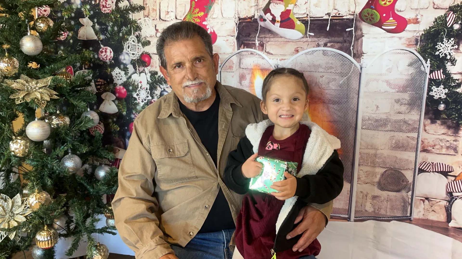 Man and young child pose with Christmas decorations, the child holding a gift.