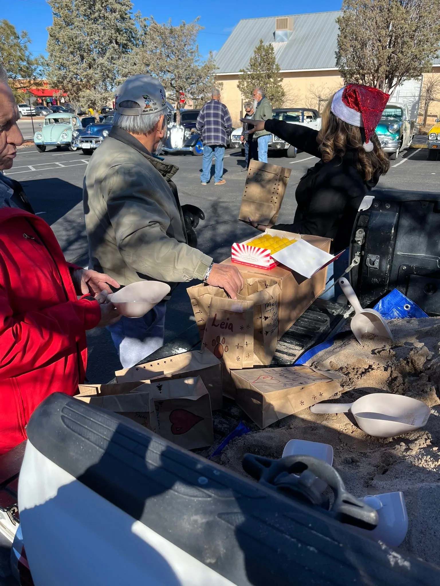 People at an outdoor event, some reaching into a cardboard box. One wears a Santa hat.