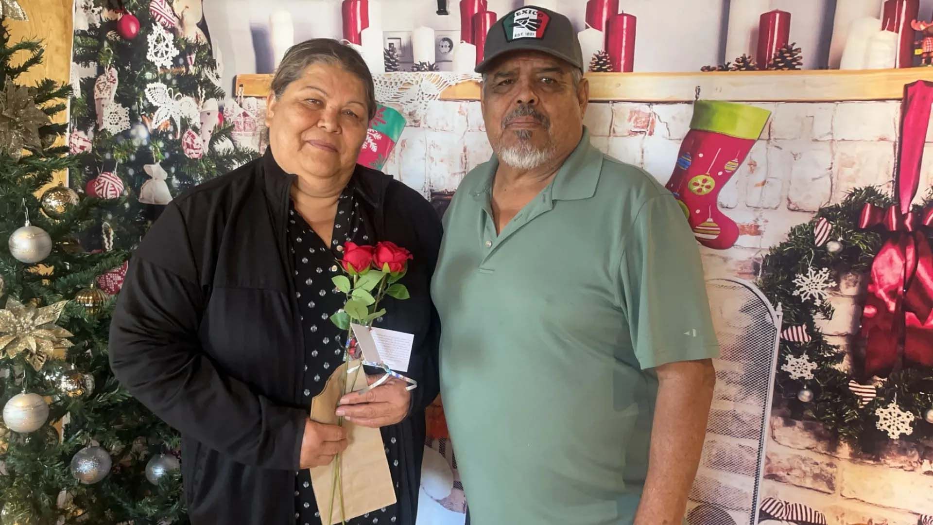 Couple posing near Christmas decorations; woman holding roses.