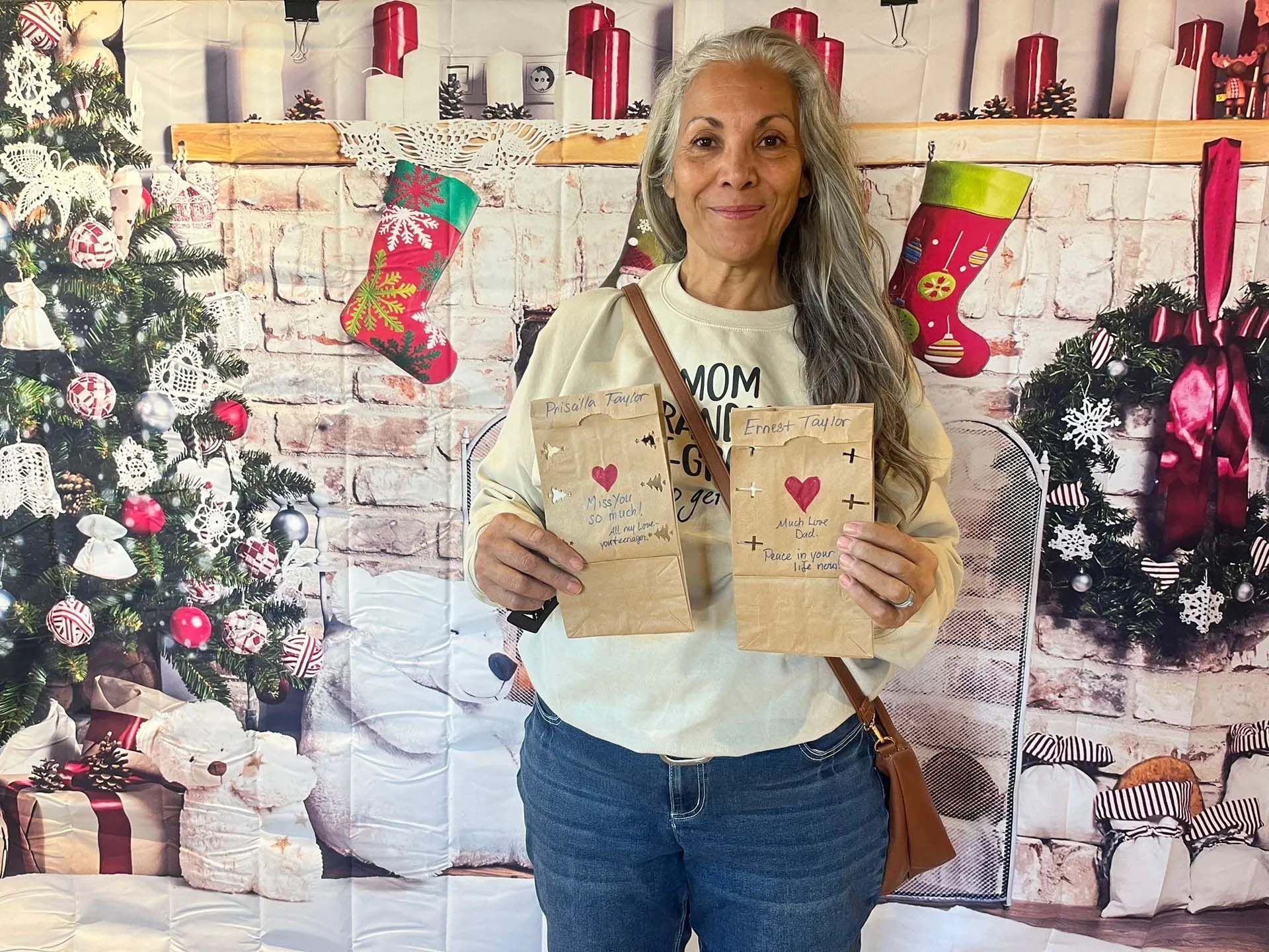 Woman holding two decorated gift bags in front of a holiday backdrop.