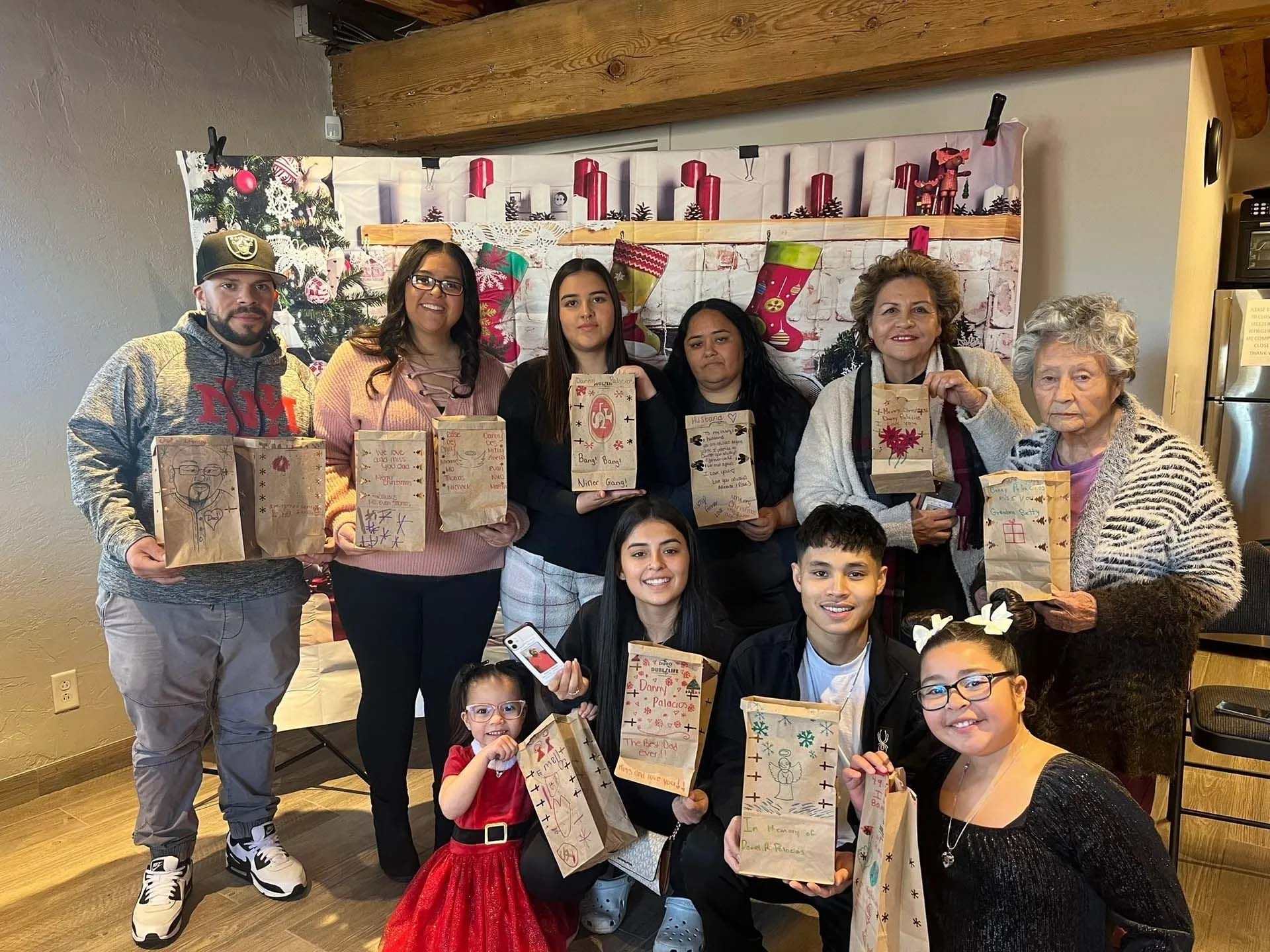 Family holding decorated paper bags in front of a Christmas backdrop.