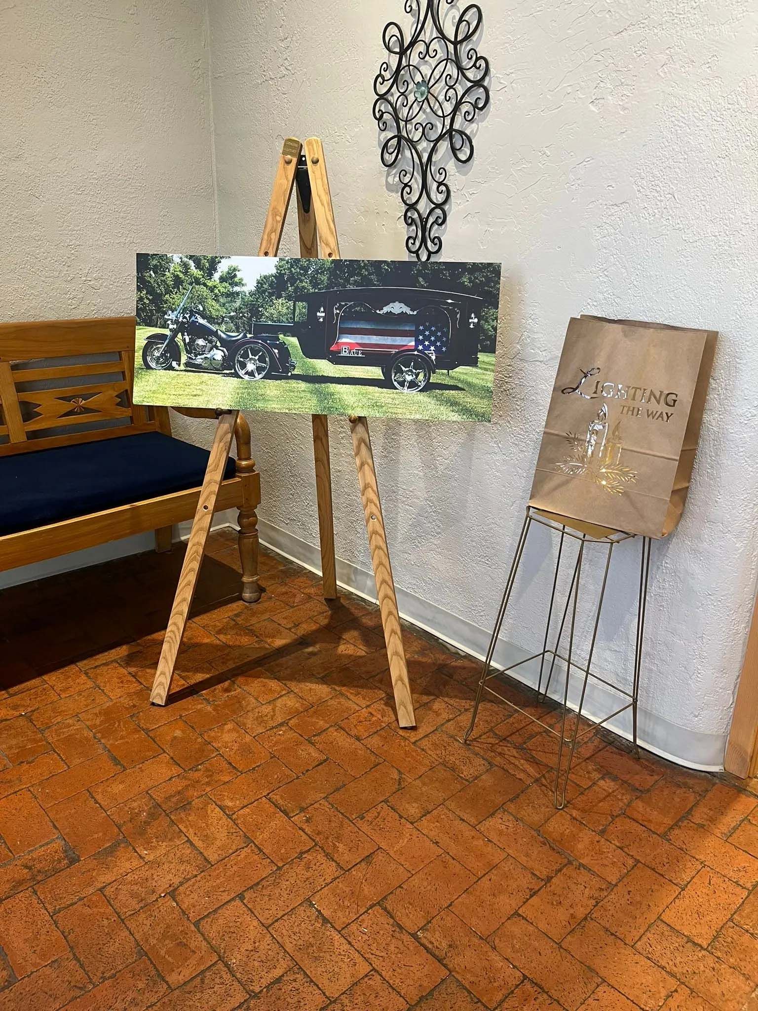 Wooden easel displays a canvas with a photo of a vehicle. A brown paper bag sits next to a smaller easel.