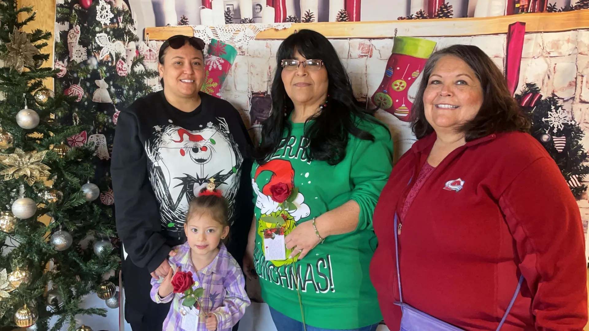 Four people pose for a photo in front of a Christmas backdrop; one person holds a rose.