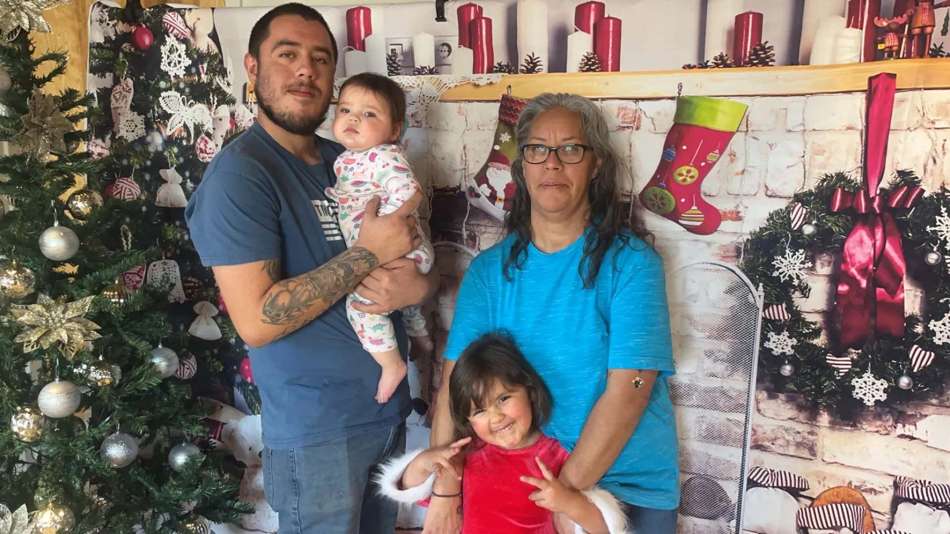 Family posing in front of a Christmas backdrop; man holding baby, woman and young girl smiling.