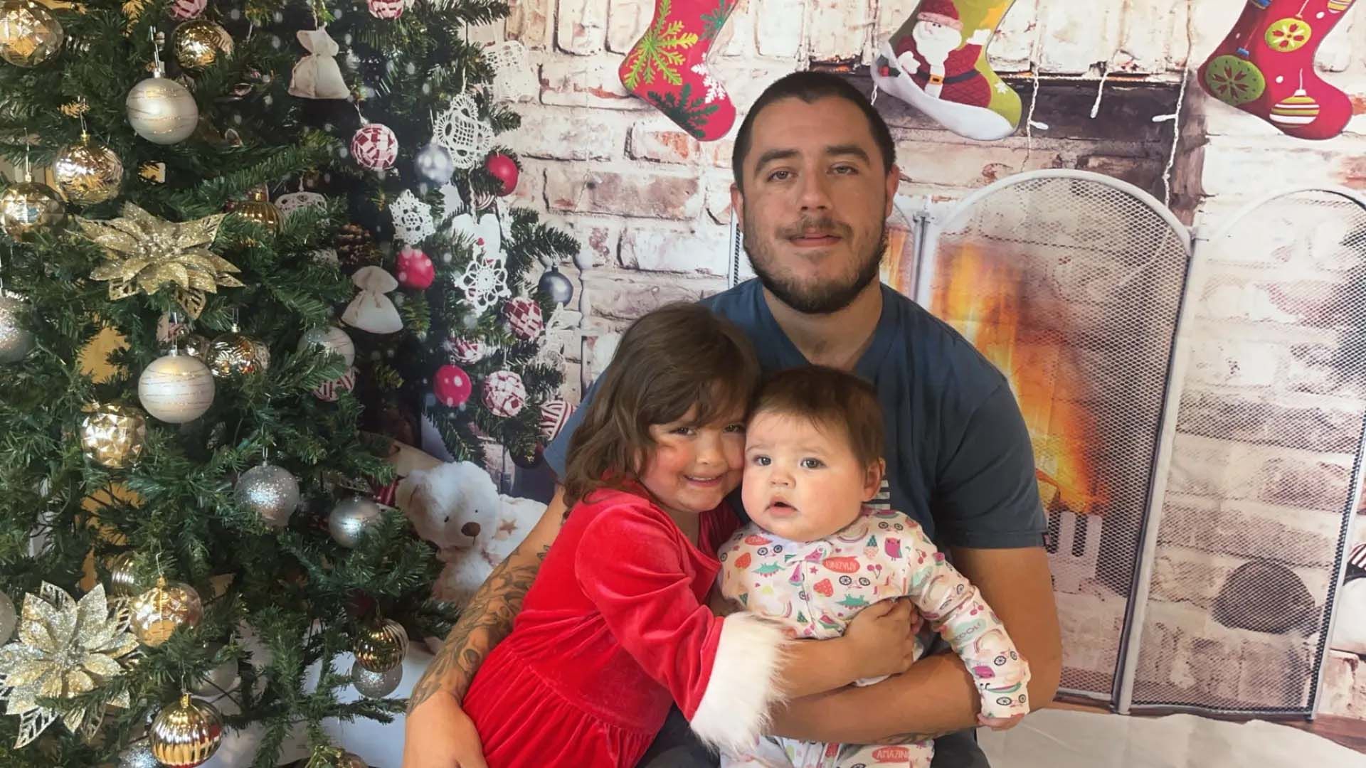 Man with two children in front of a Christmas tree and fireplace backdrop.