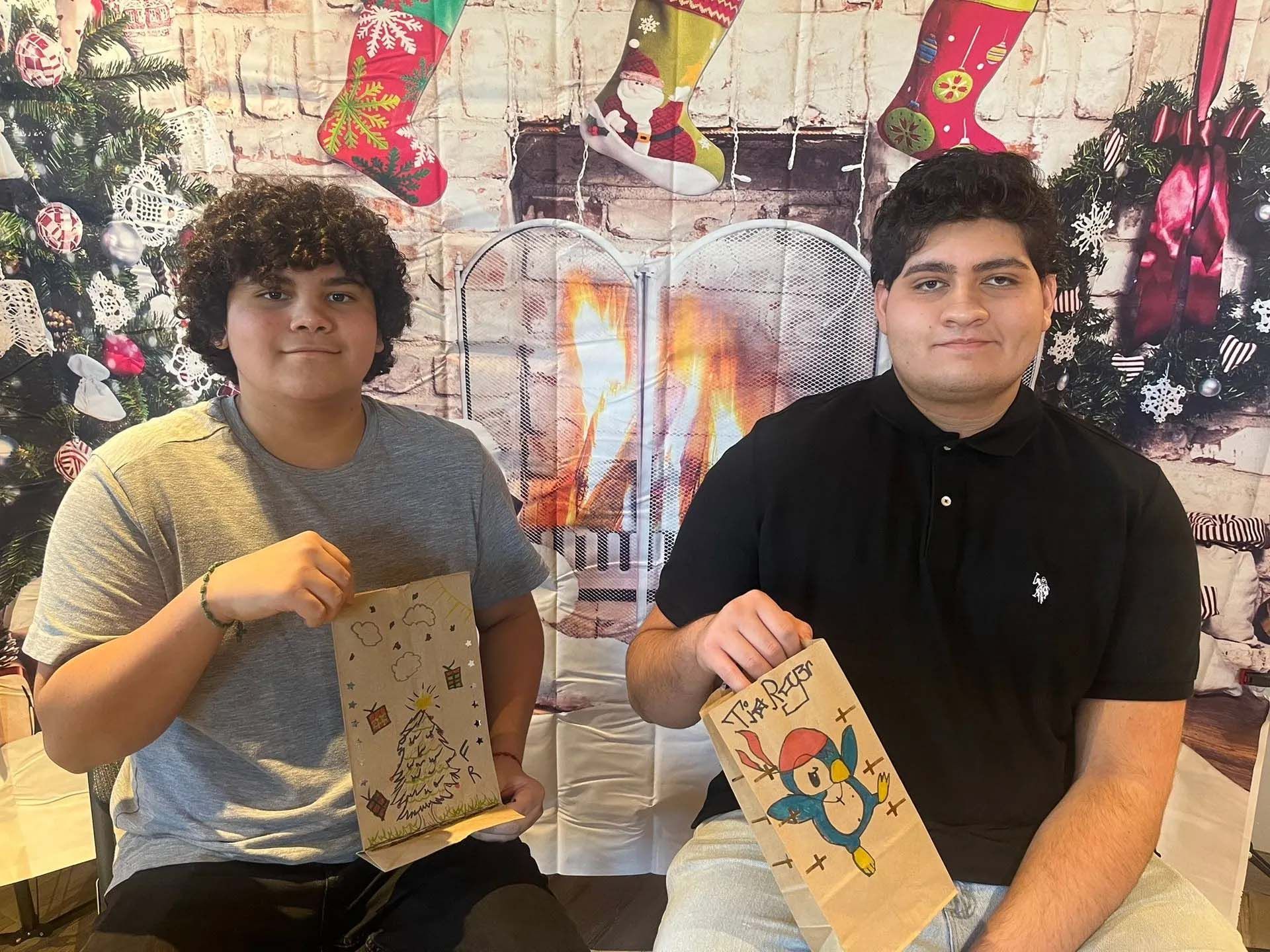 Two people holding decorated paper bags with a holiday backdrop.