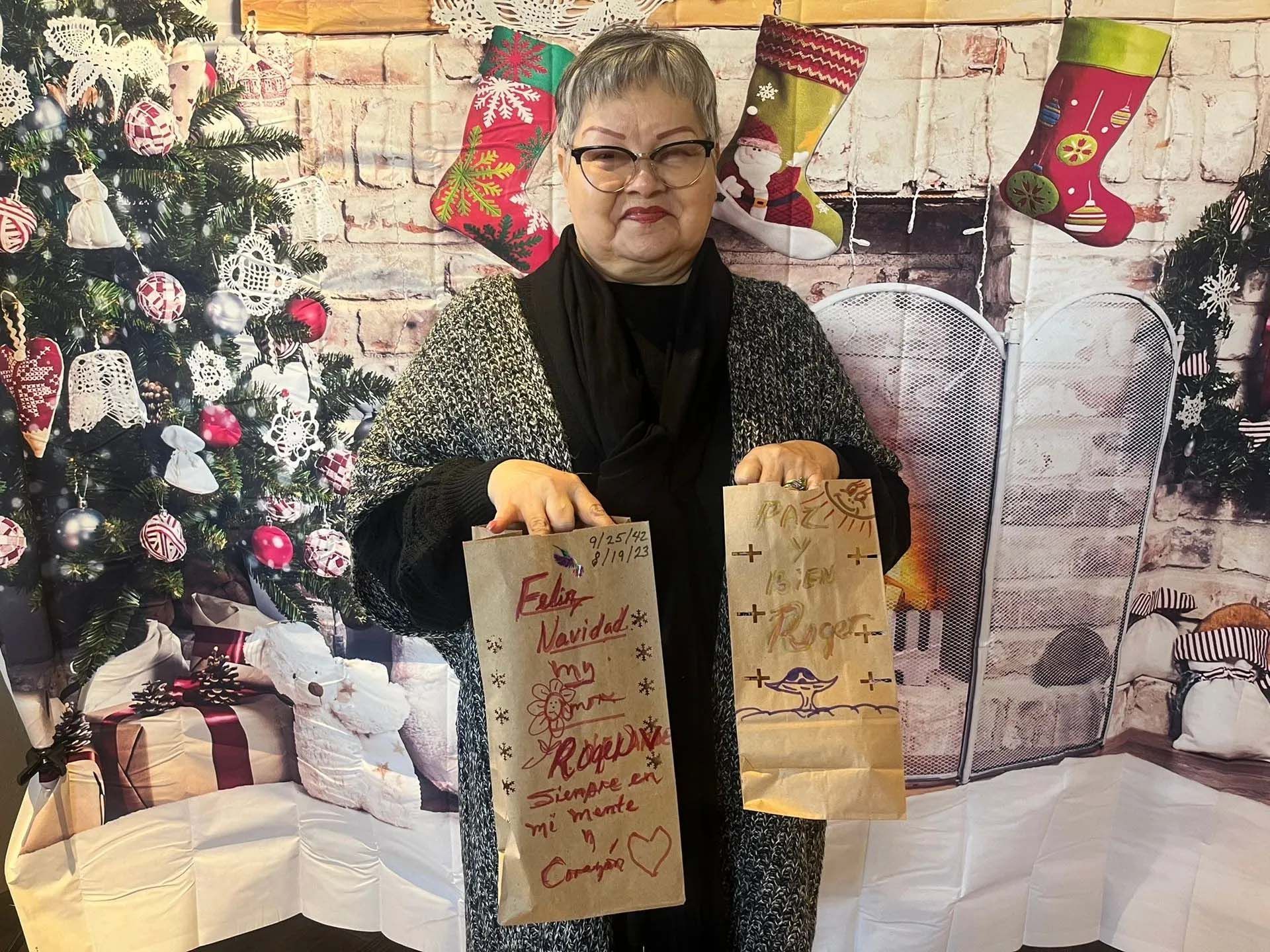 Woman holding decorated bags, in front of a Christmas backdrop.