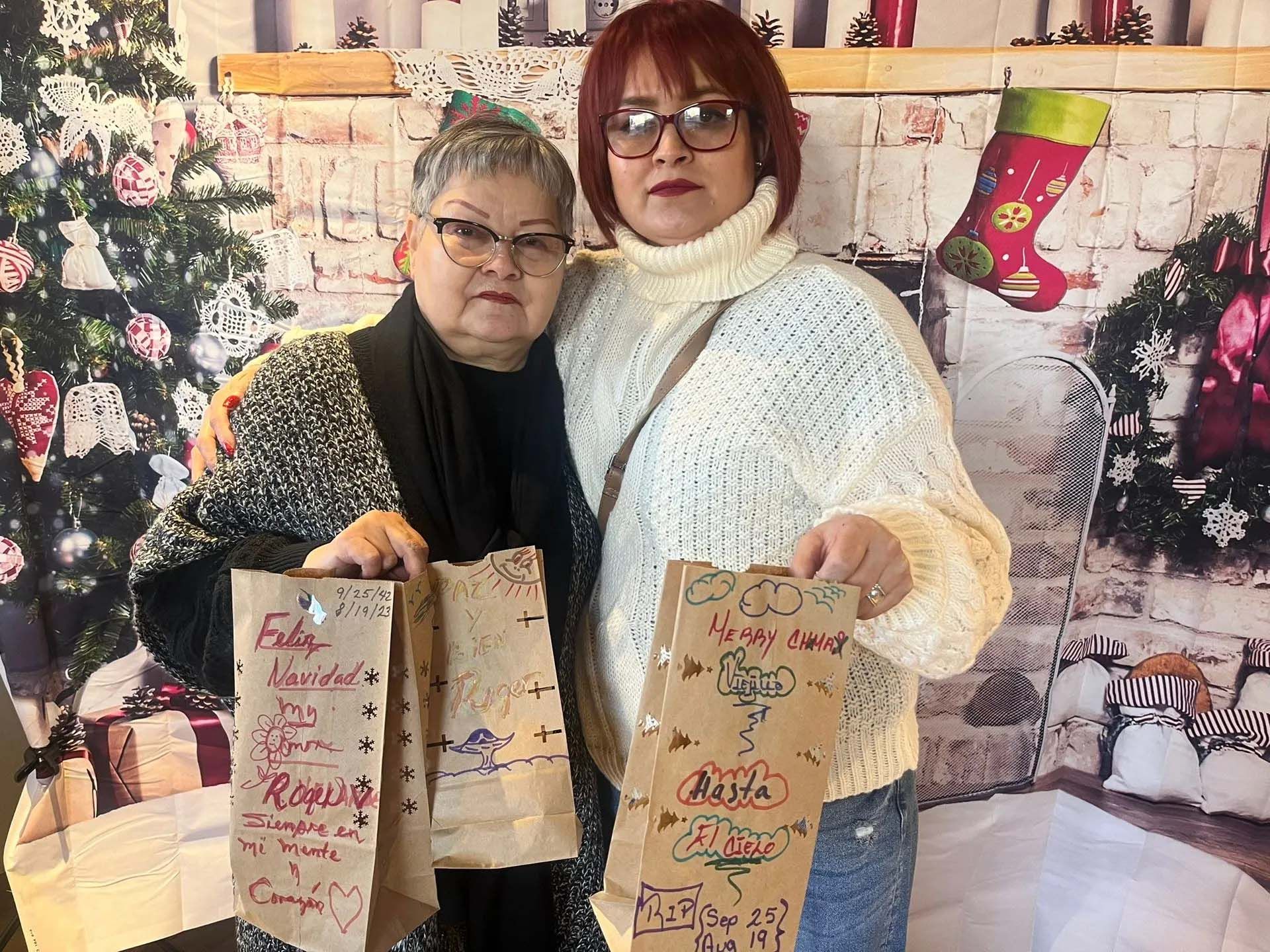 Two women with decorated bags, posing in front of a holiday backdrop.