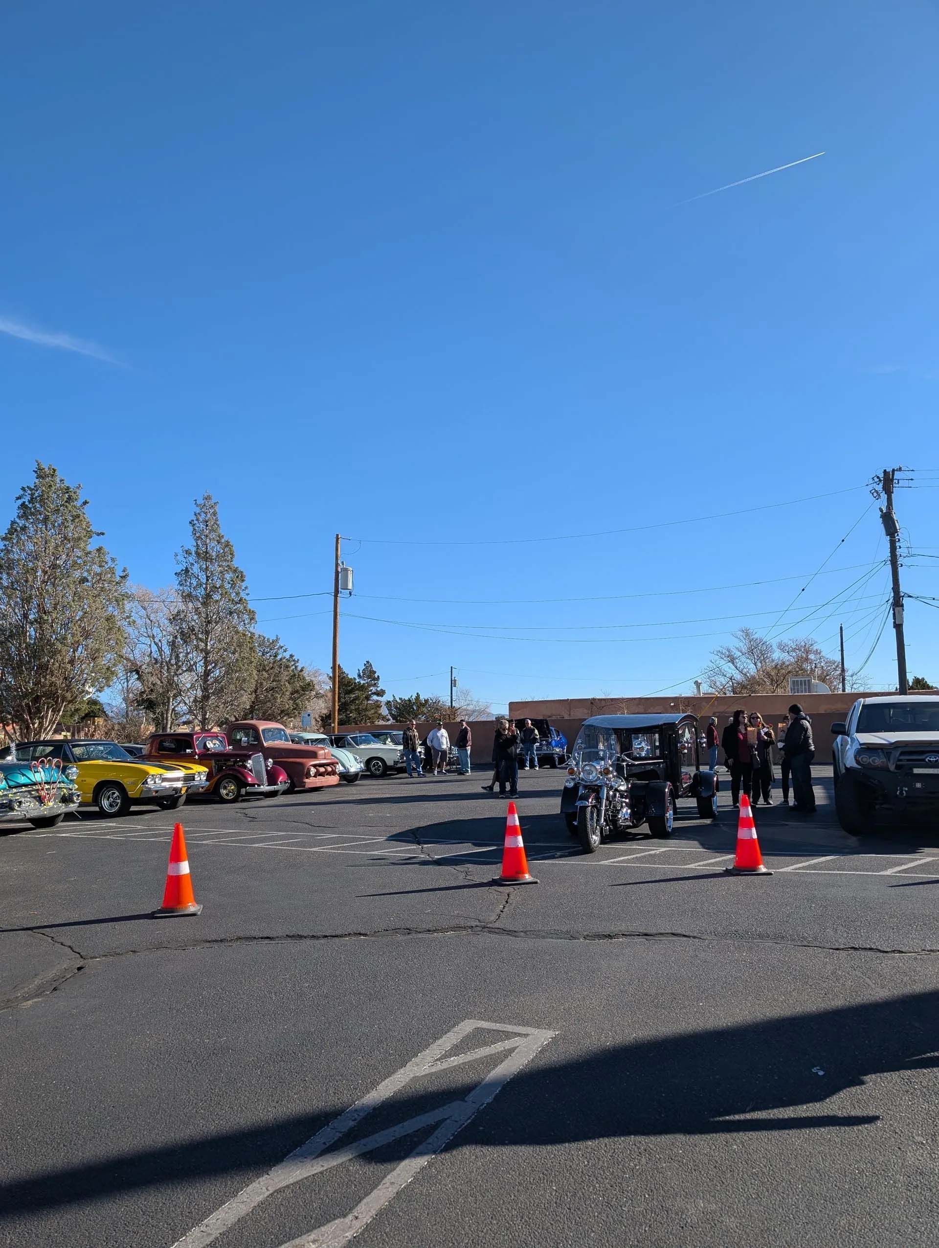 Cars parked in a lot under a clear blue sky; traffic cones in the foreground.