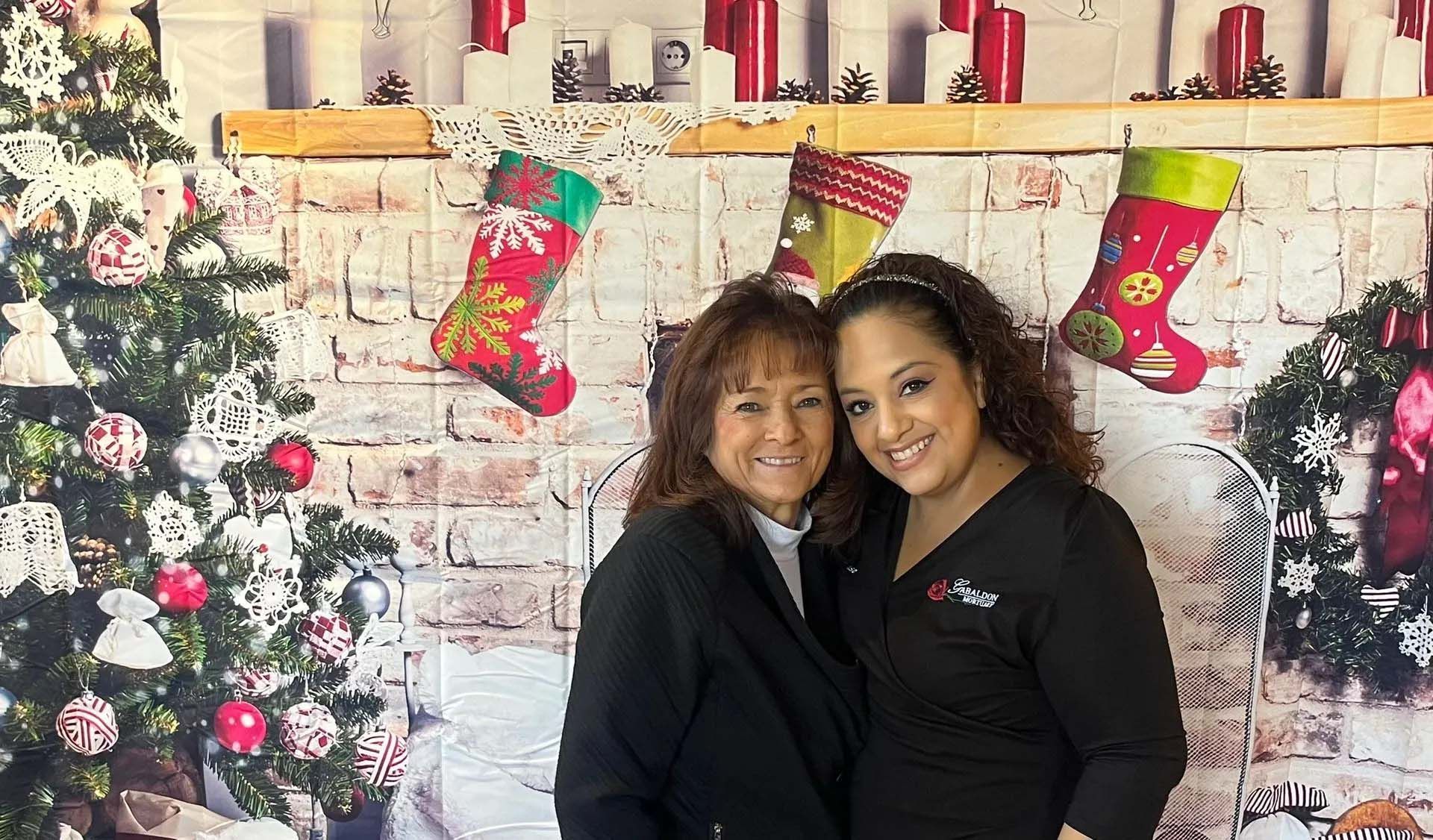 Two smiling women pose in front of a Christmas-themed backdrop.