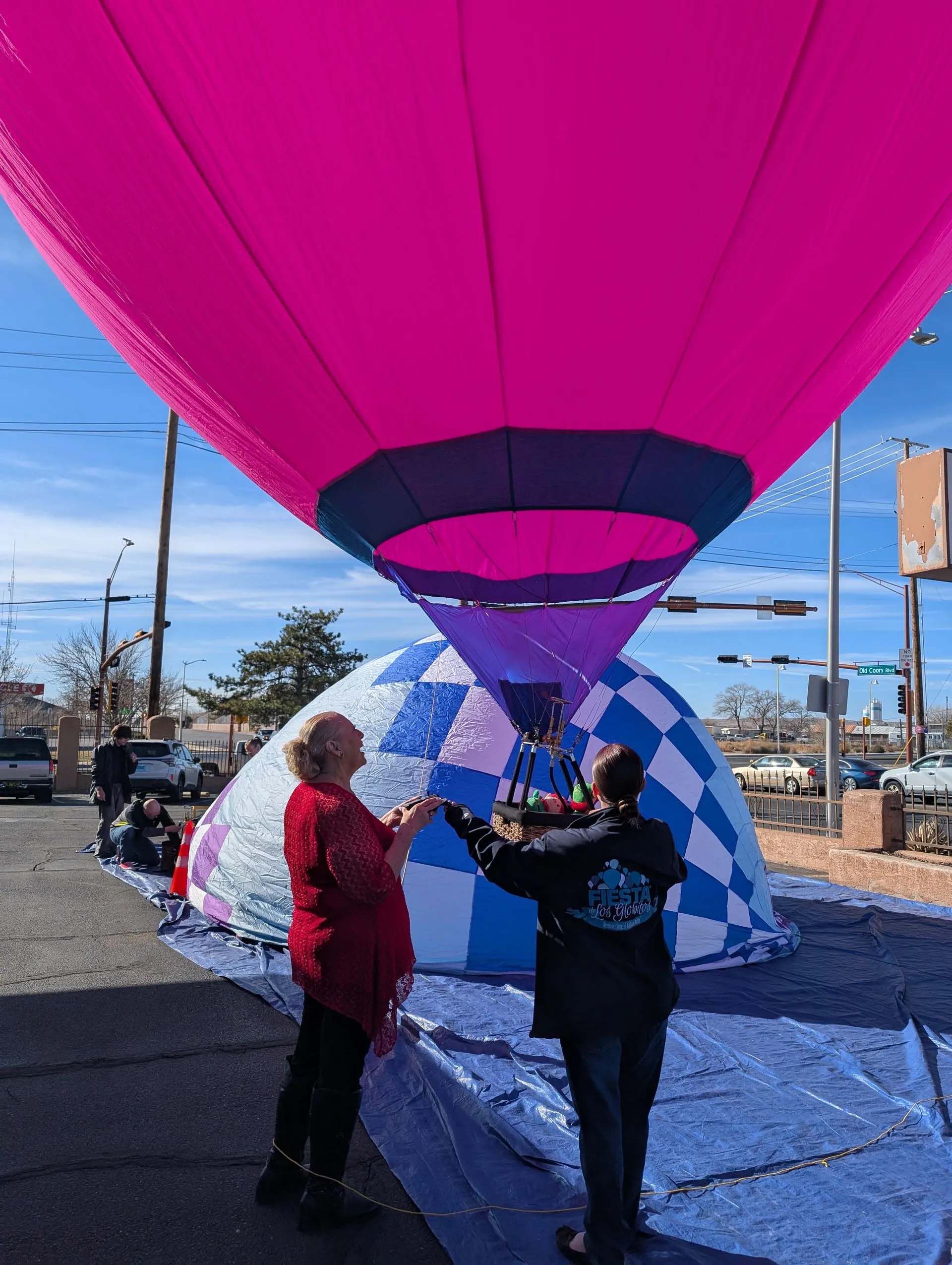 Two people preparing a pink and blue hot air balloon. City street setting.