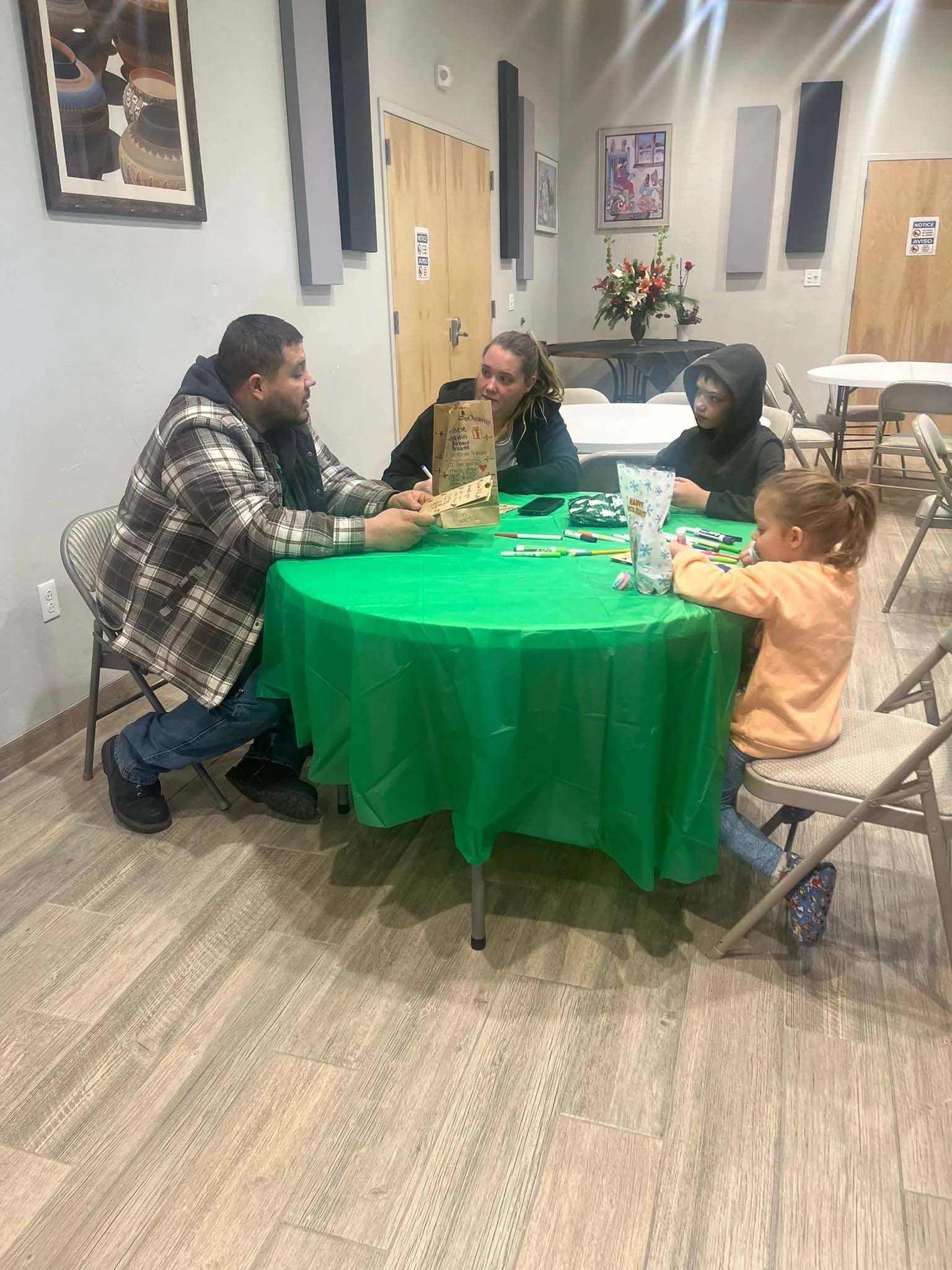 Four people seated around a green table playing a game, indoors.
