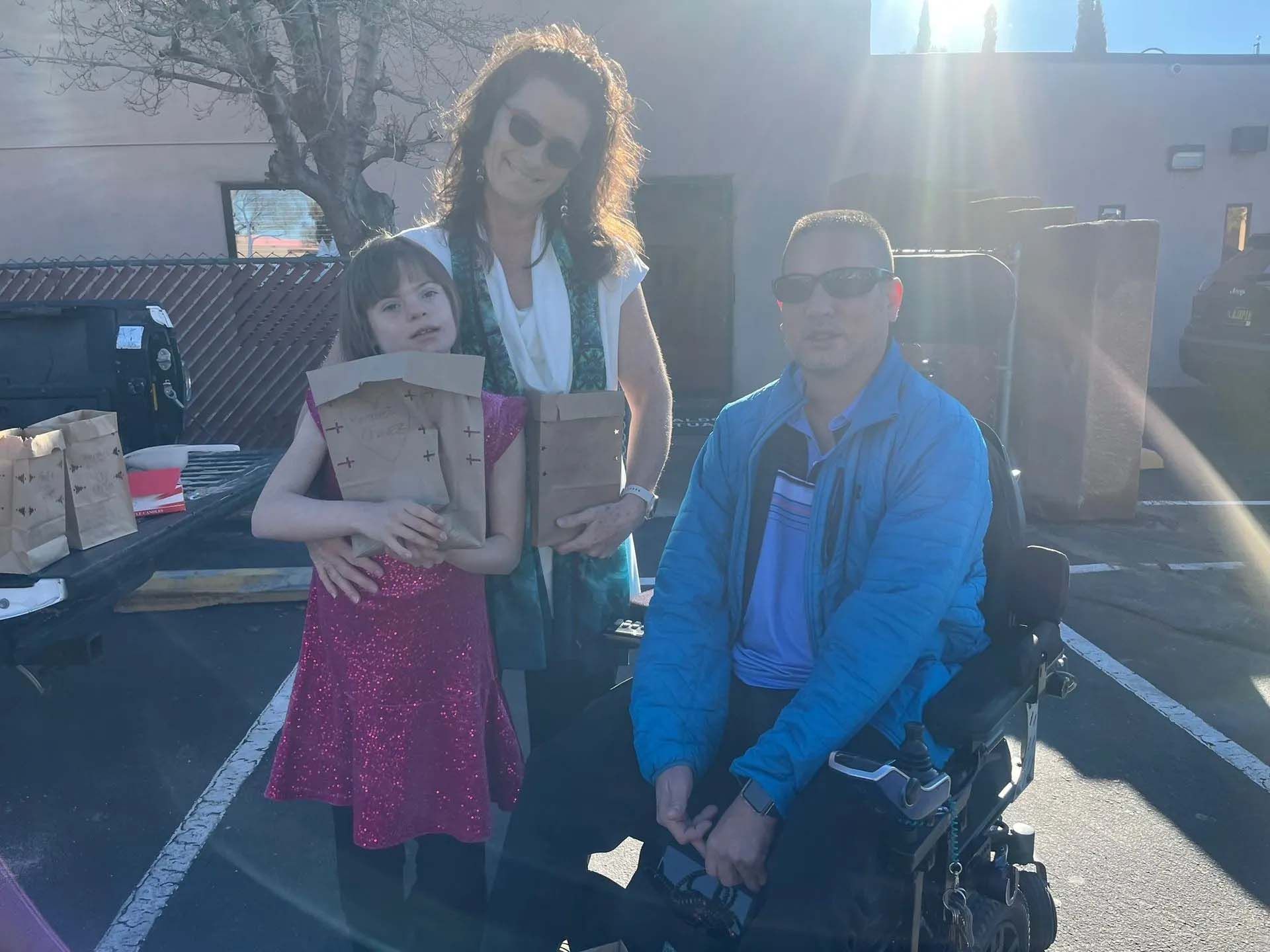 Woman and child holding paper bags with a person in a wheelchair in front of a building.