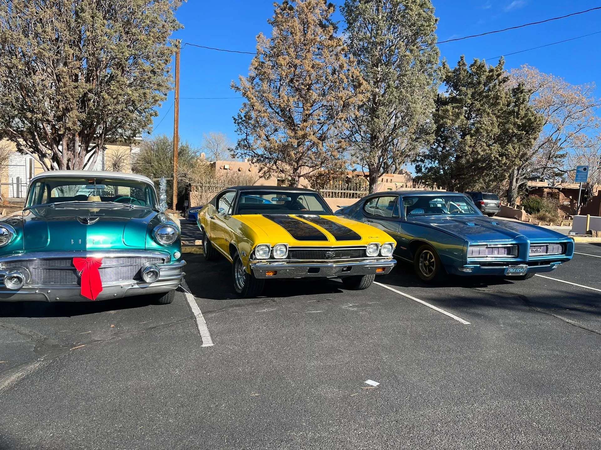 Three classic cars parked outside: teal, yellow with black stripes, and blue.
