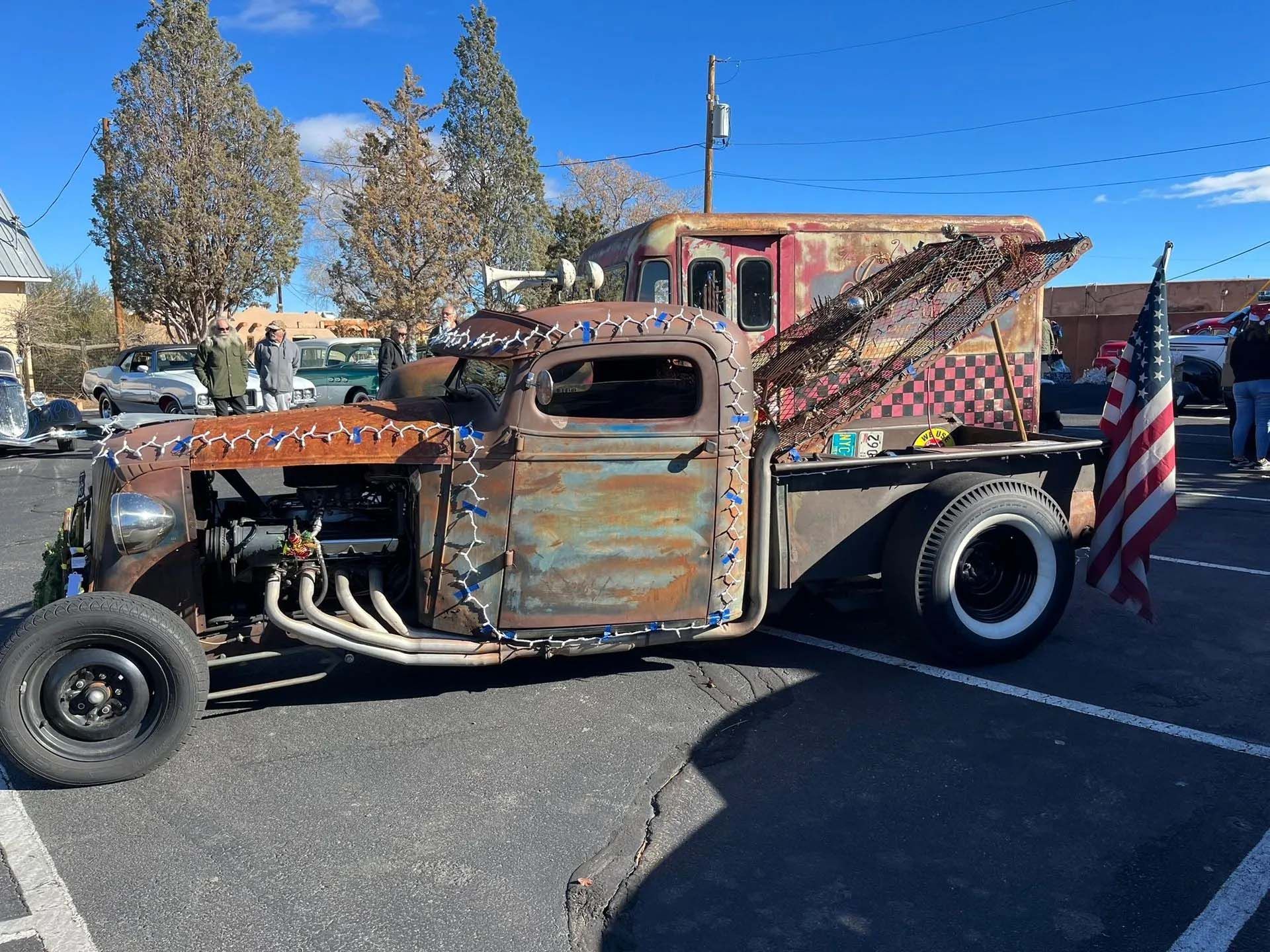 Rusty vintage tow truck with American flag, displayed at an outdoor car show.