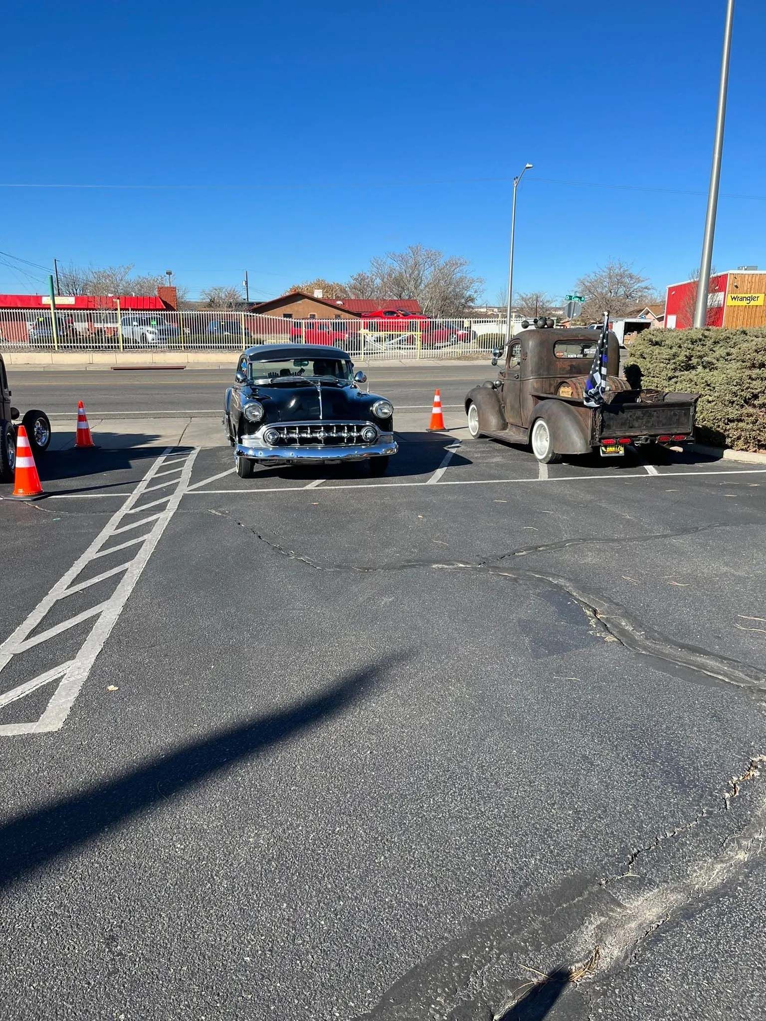 Classic car and flatbed tow truck in a parking lot on a sunny day.