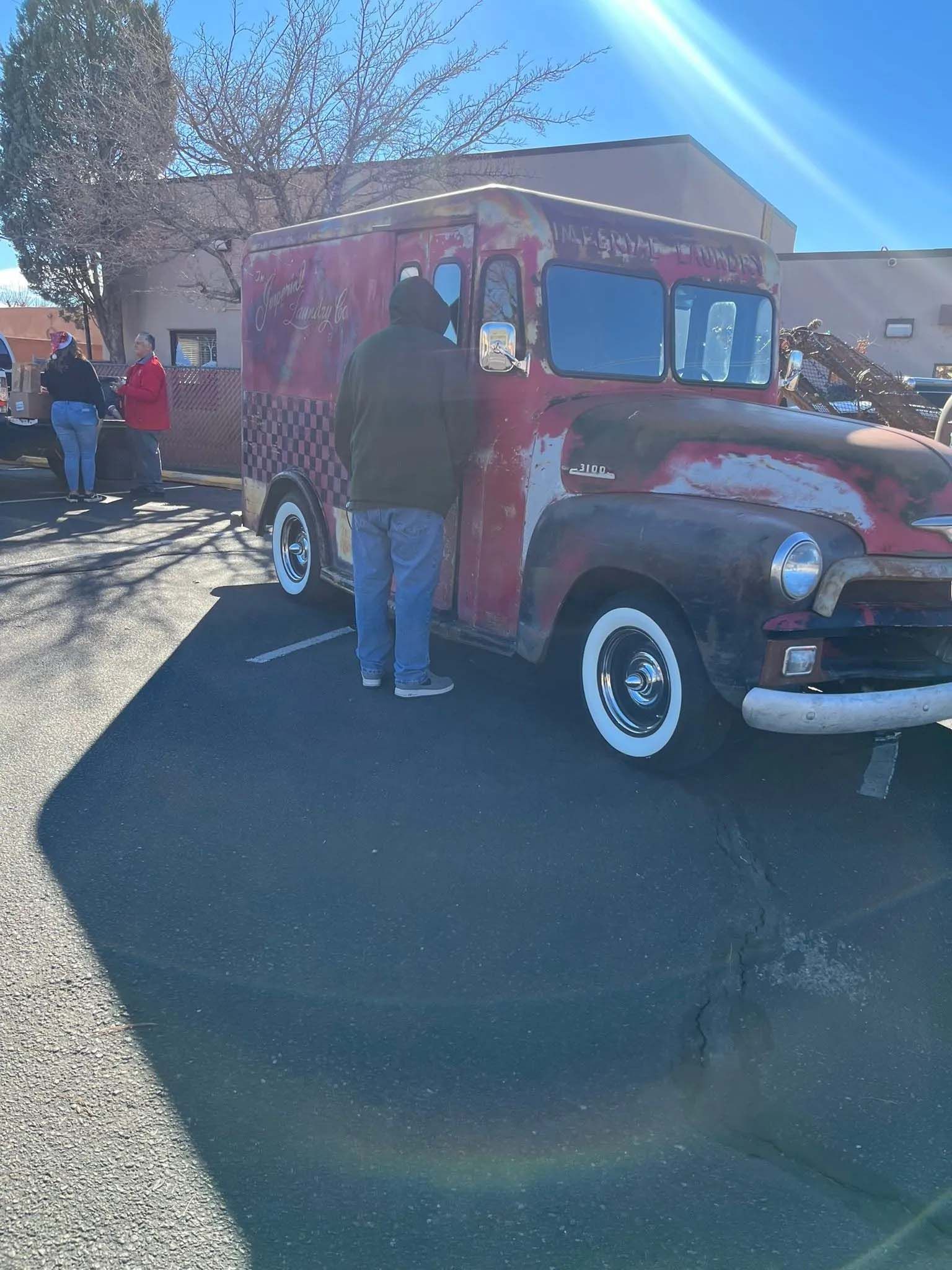 A red, vintage truck with white-walled tires parked outside; a man stands near it.