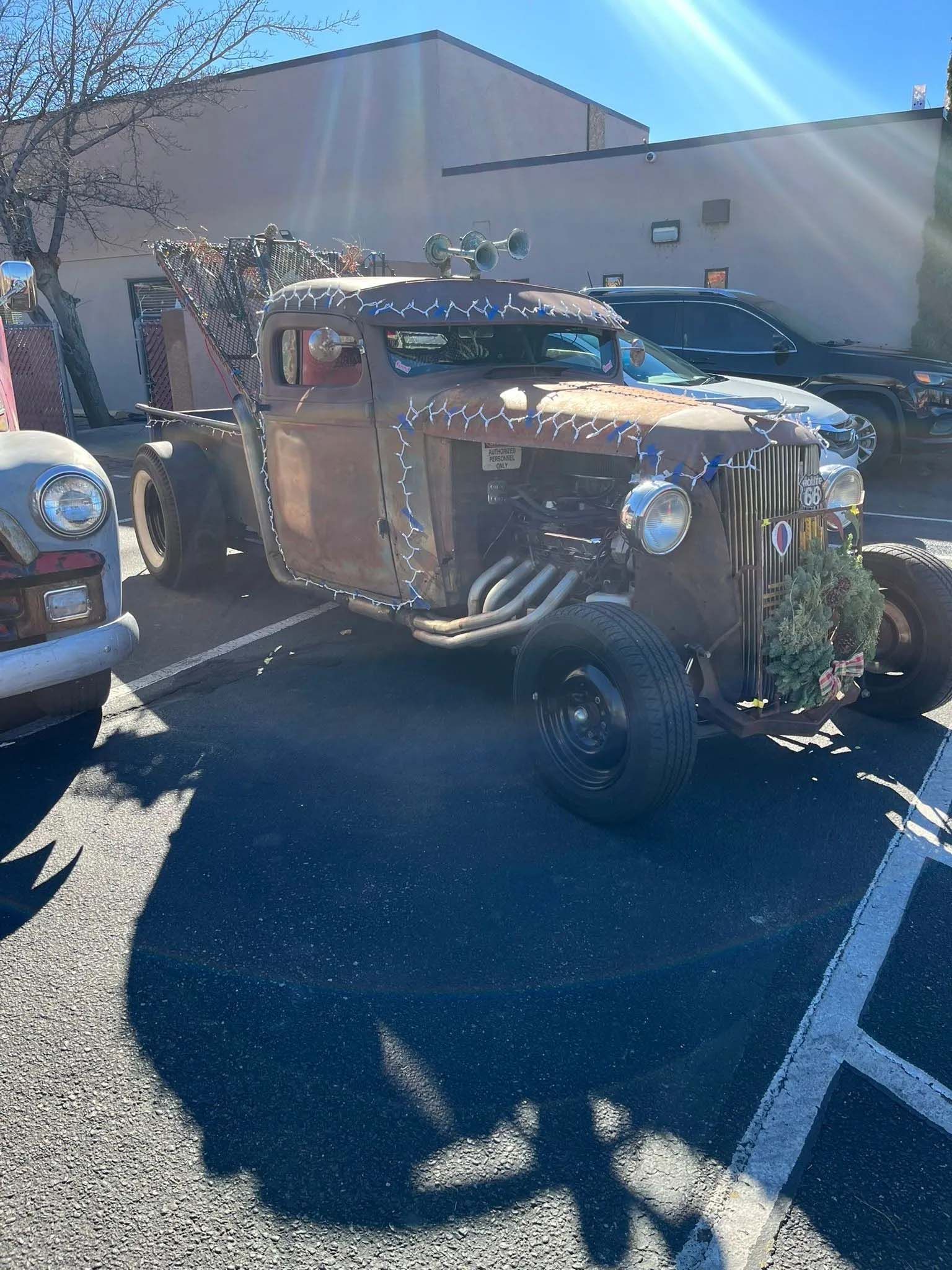 Rusty, modified truck with exposed engine, decorative lights, parked outside.