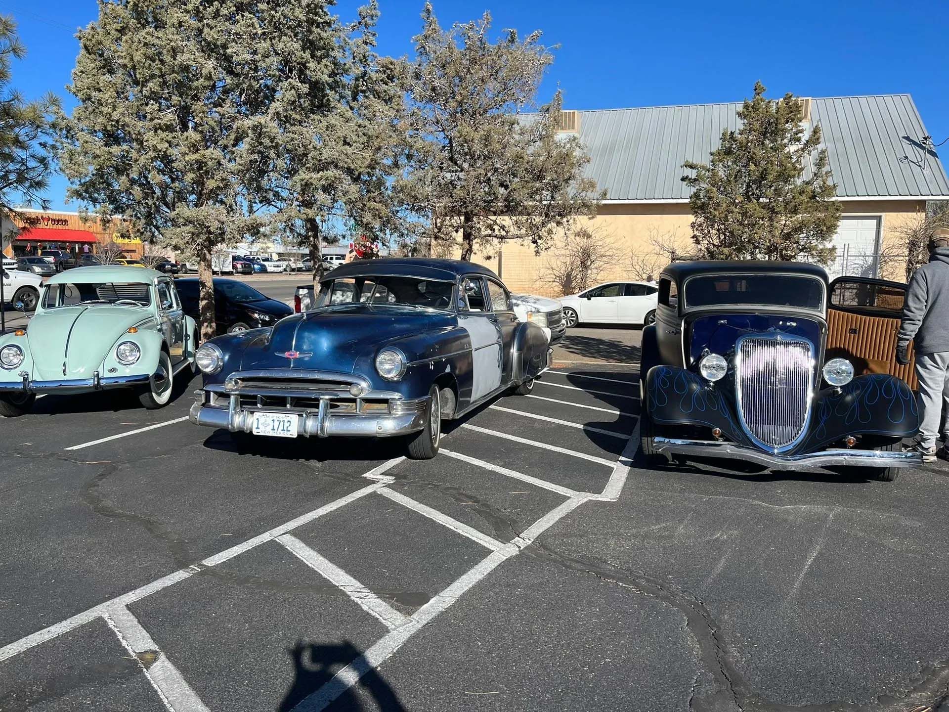 Classic cars parked outdoors, including a blue Beetle, a navy sedan, and a dark blue coupe.
