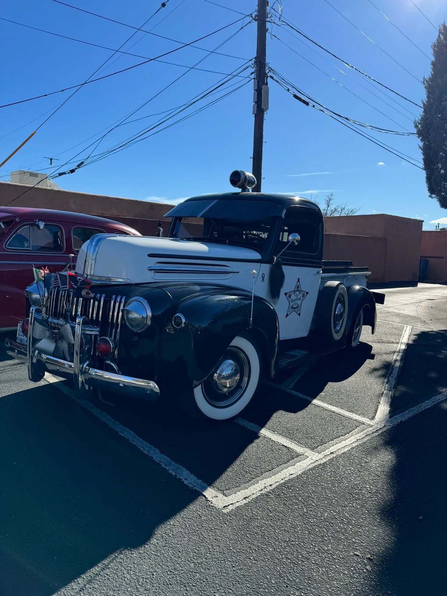Vintage black and white Sheriff's pickup truck parked in a lot under a clear blue sky.