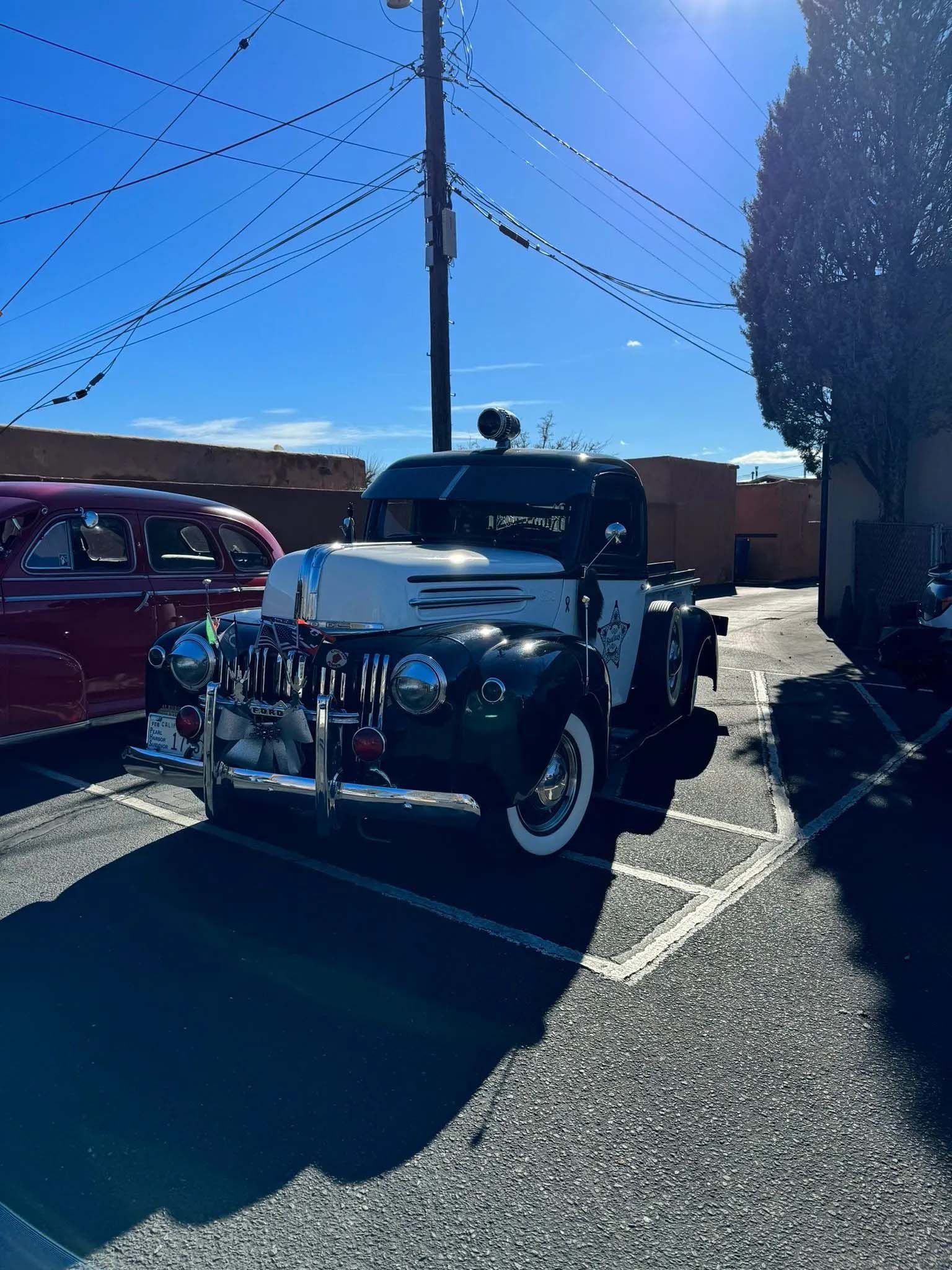 Vintage black and white police truck parked in a lot under a clear blue sky.