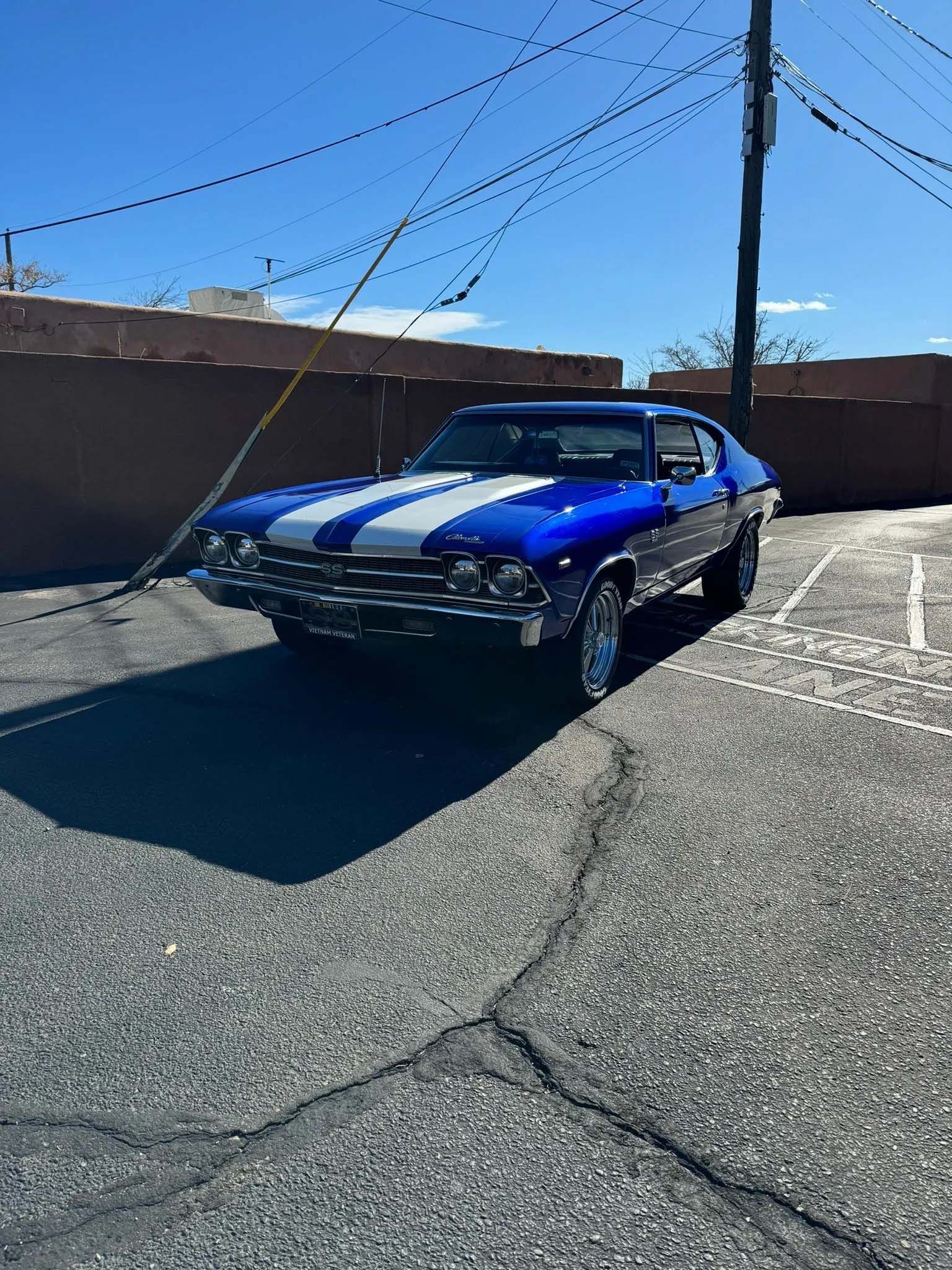 Blue classic car with white racing stripes parked in an alley on a sunny day.