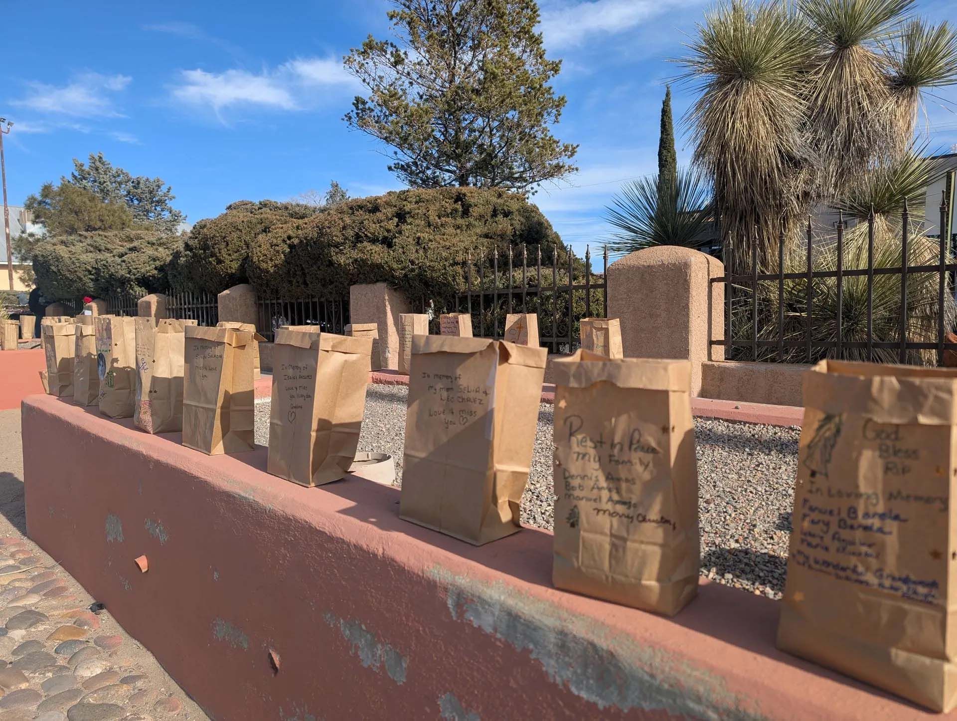 Brown paper bags on a red wall, possibly for a memorial or display, against a blue sky.