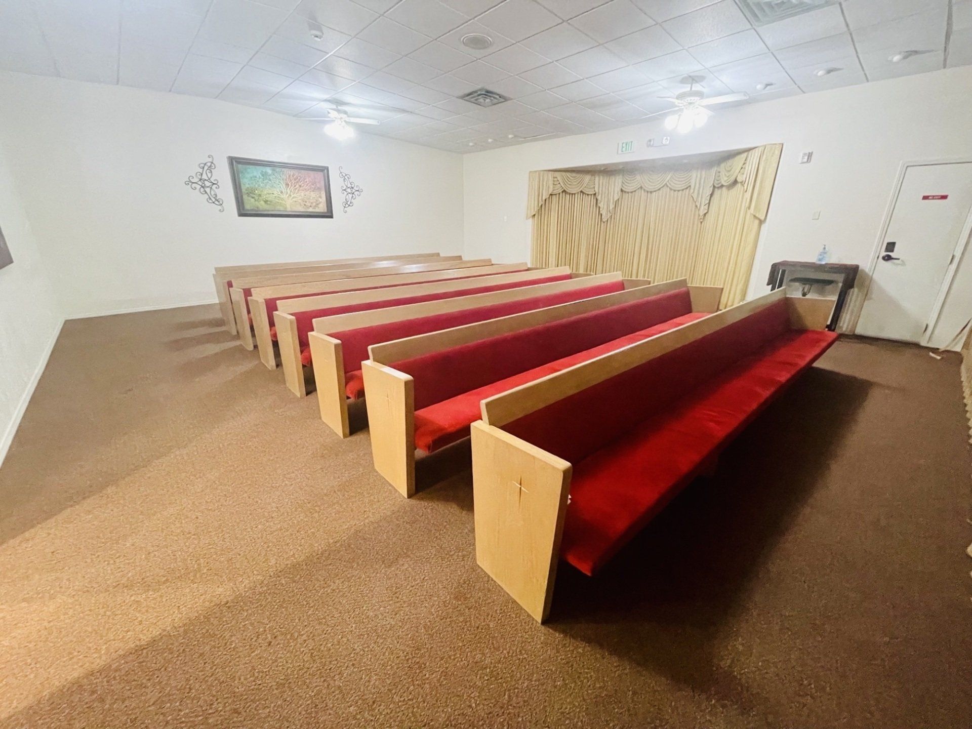 Rows of wooden pews with red cushions in an empty room, presumably a chapel.