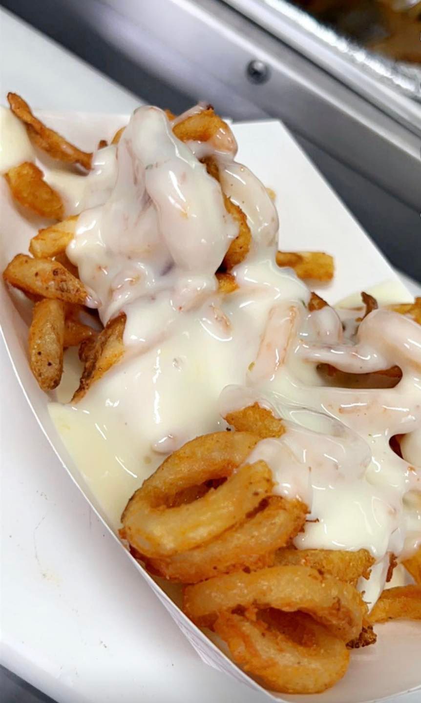 a paper container filled with waffle fries and cheese sauce .