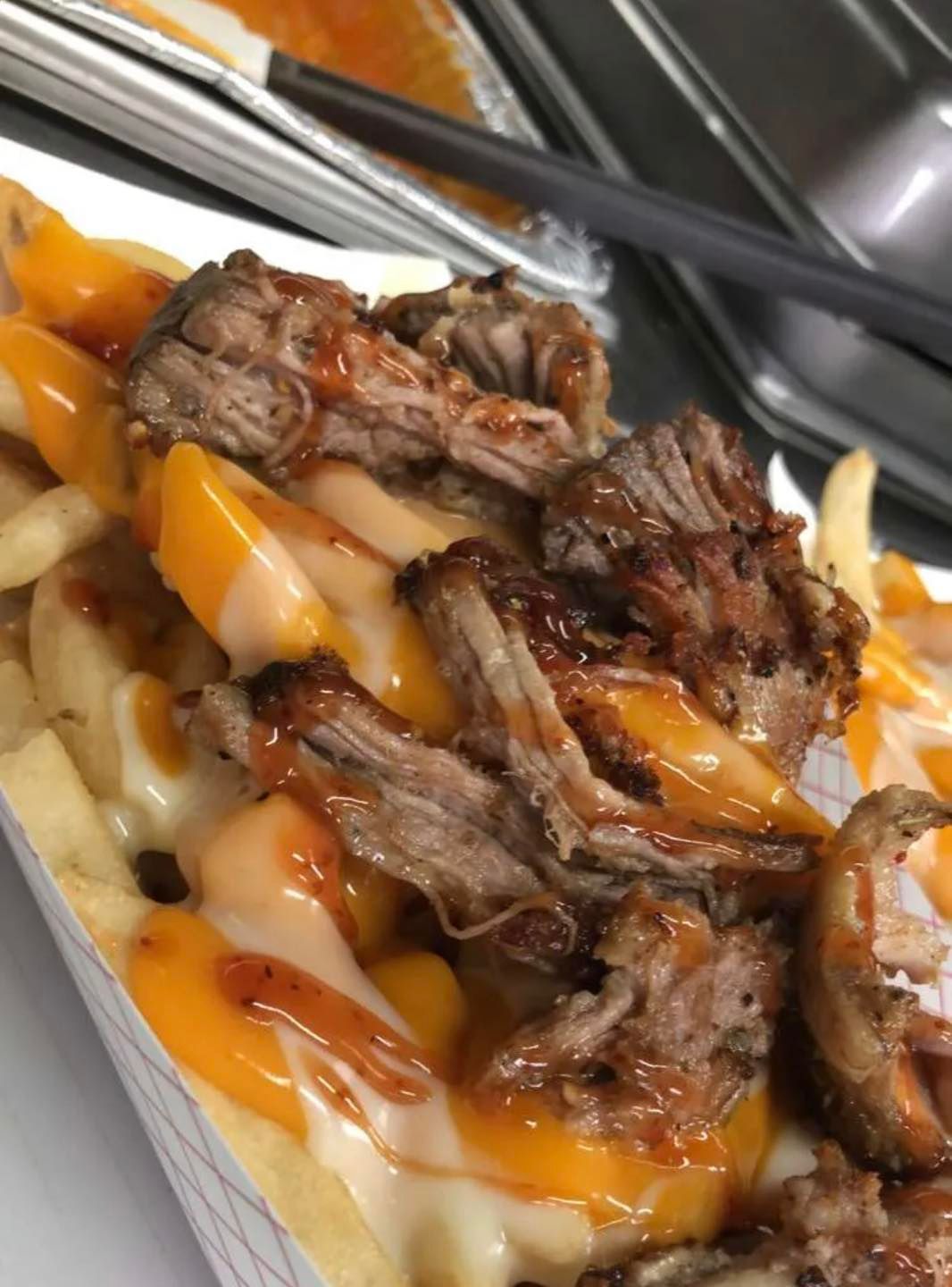 a tray of pulled pork fries with cheese and sauce