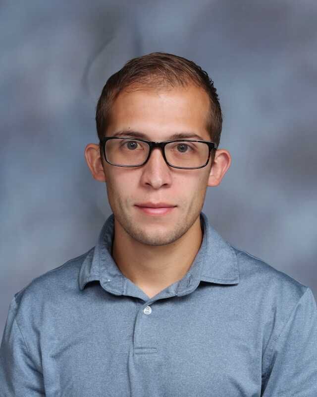A man wearing glasses and a blue shirt is posing for a picture.