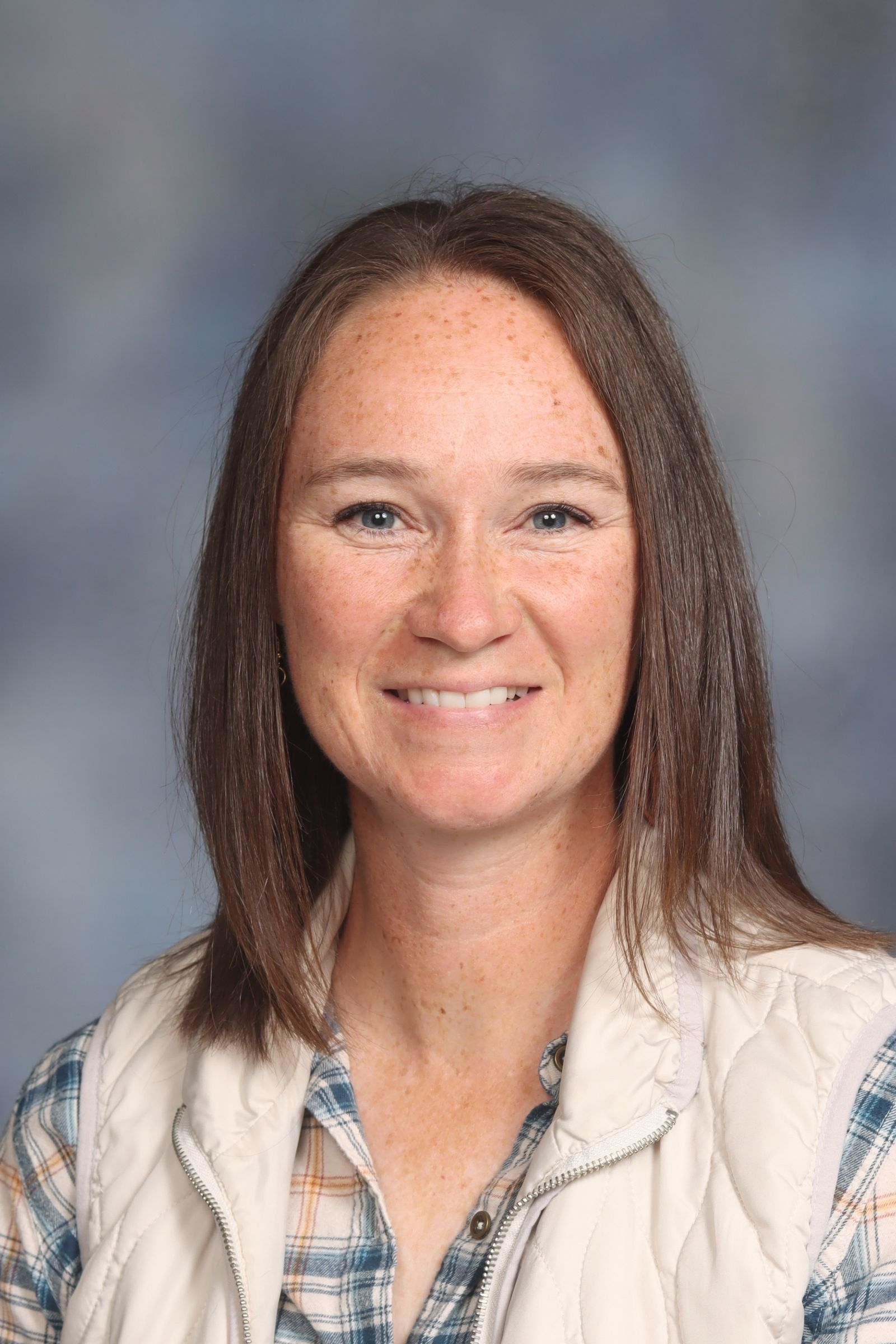 A woman in a yellow floral shirt is smiling for a picture.