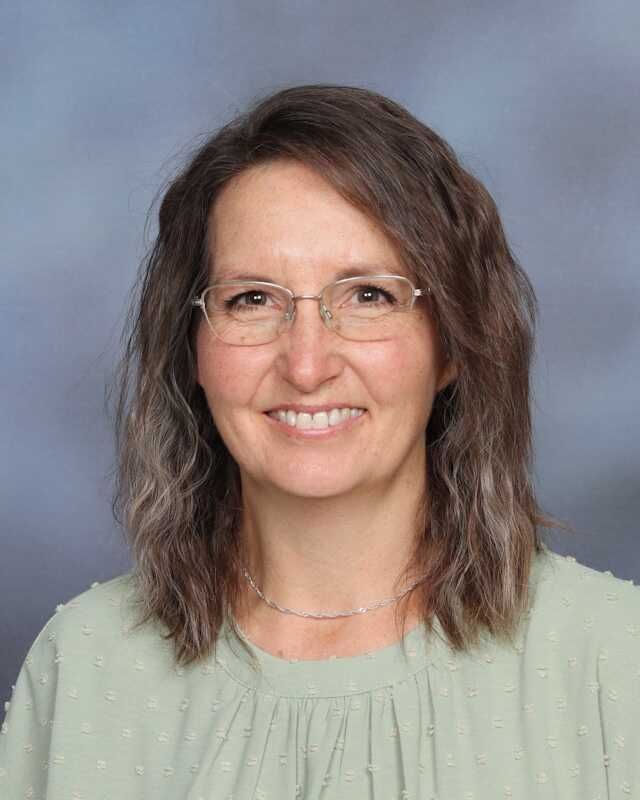 A woman wearing glasses and a green shirt is smiling for the camera.