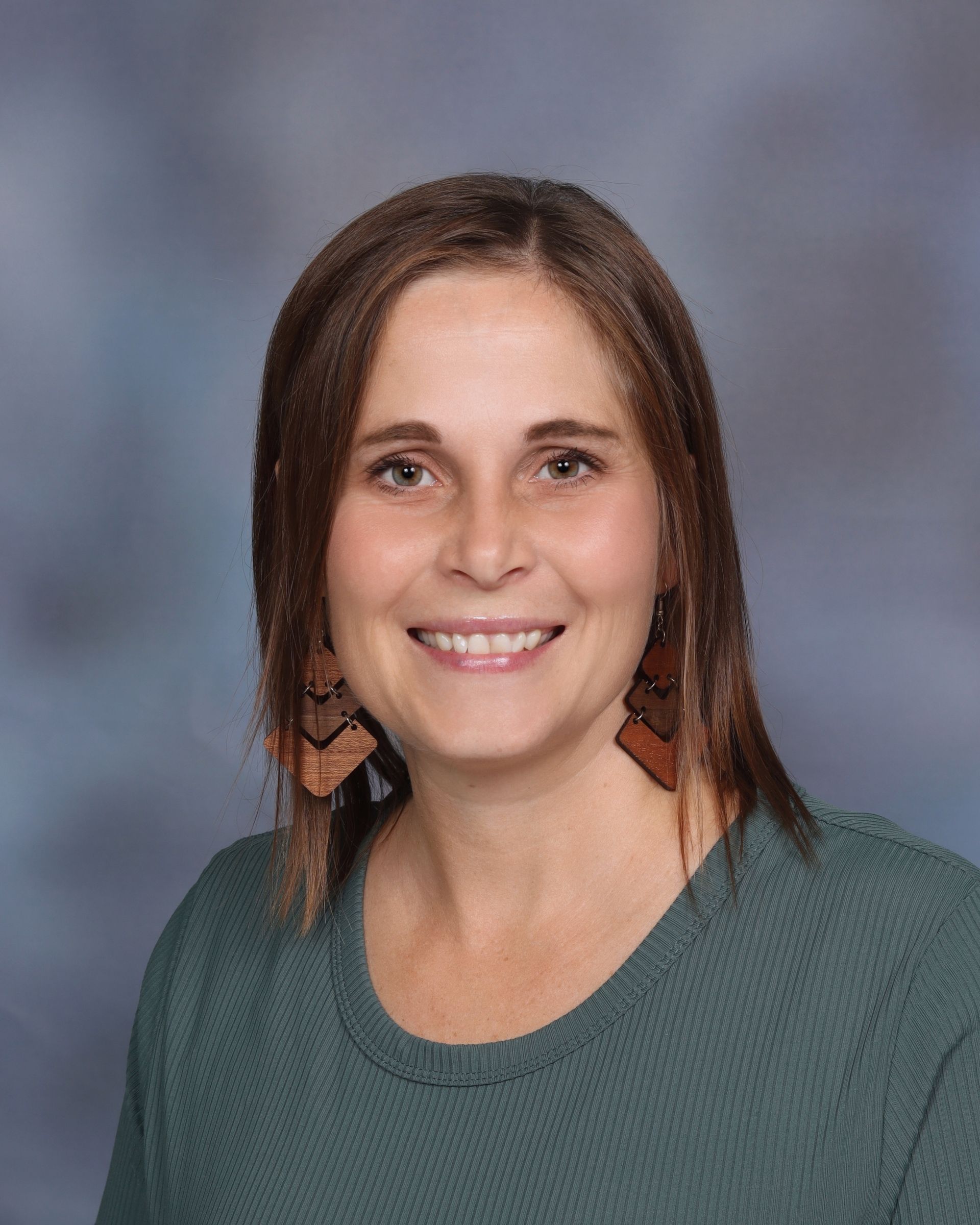 A woman in a white shirt and earrings is smiling for a picture.